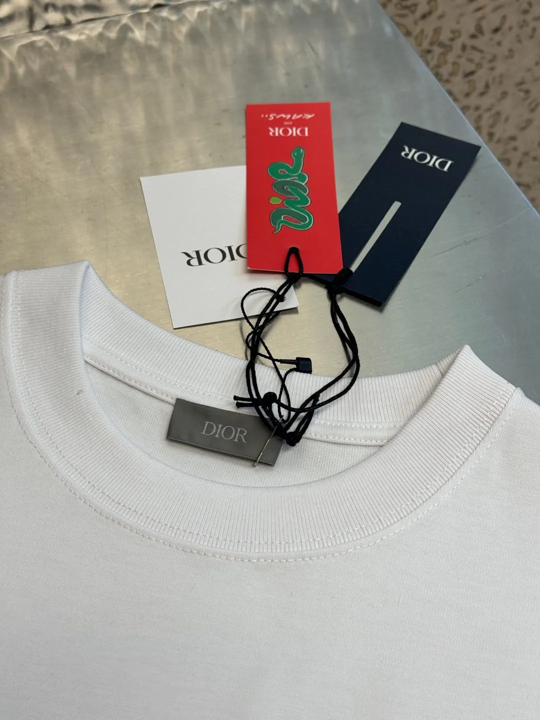 🅿️280 Dior Apple Snake Embroidered Chapter Short Sleeve Made of pure cotton 12S fine cotton plain fabric, 310g. The embroidery pattern is based on tatami embroidery technology. The embroidery uses a special single-needle arrangement. The stitches are tight and flat, forming a texture similar to the tatami grid, making the embroidery pattern have a strong three-dimensional and layered feel. Embroidered with silk threads of multiple colors, the colors are bright and contrasting, showing rich patterns and details.  The outline is stroked by needle embroidery, the embroidery pattern is matched with the brand logo design, and the brand letter logo is single-needle flat embroidered. Made from a variety of needlework; the outline of the pattern is embroidered with a single straight line and straight silk thread. The outline edges and letter embroidery are stitched together to create clear and rich three-dimensional layers.  The standard round neck and short-sleeved version has a rounded arc neckline, which is suitable for various face shapes and body shapes; the sleeve length is moderate and ends just above the elbow, showing a smart and neat image. The slim fit can show off the wearer's body curves without sacrificing comfort. The collar, cuffs, hem and other parts are all sewn with fine double-needle stitching.  size：xs s m l