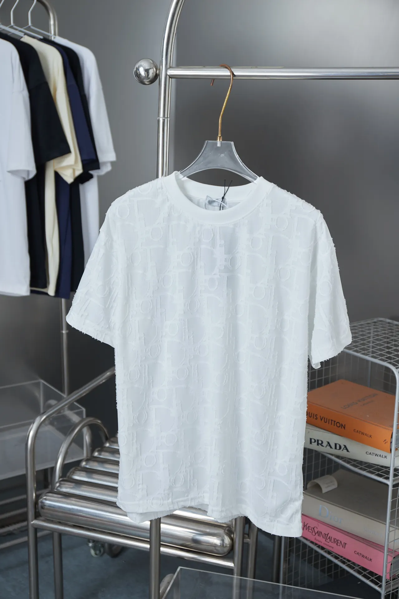 🅿️180 Dior 2025 new style embossed jacquard short-sleeved pure cotton plain fabric, woven with 32S double-strand pure cotton yarn. The 32S double-strand is twisted from two 32-count single yarns. The yarn is thicker and stronger. The fabric has high wear resistance while retaining the moisture absorption and breathability of pure cotton. The plain weave has a tight structure and a smooth surface, but it feels relatively stiff and supports the stiffness of the pattern. The jacquard pattern uses thread-cutting jacquard technology, and the full-width Oblique jacquard pattern forms a relief effect through the deep integration of full-width jacquard and shearing technology. The jacquard structure provides a three-dimensional frame, and the shearing process enhances local texture. The electronic jacquard machine is used to weave complex patterns on the entire fabric to form a three-dimensional concave and convex texture, achieving the integration of texture and pattern. The raised jacquard is cut in a directional manner to create a relief effect, enhancing tactile layering and visual contrast. Straight crew neck fit. Cut and sewn in floral position, standard H hanging fit, with shoulder-length design. The vertical version emphasizes that the width of the shoulders, waist, and hem are basically the same, and it is simple and loose. The short sleeves are tailored to fit the body of the wearer. At the same time, the neckline, cuffs and hem of the short sleeves are all designed with double lines. S M L XL
