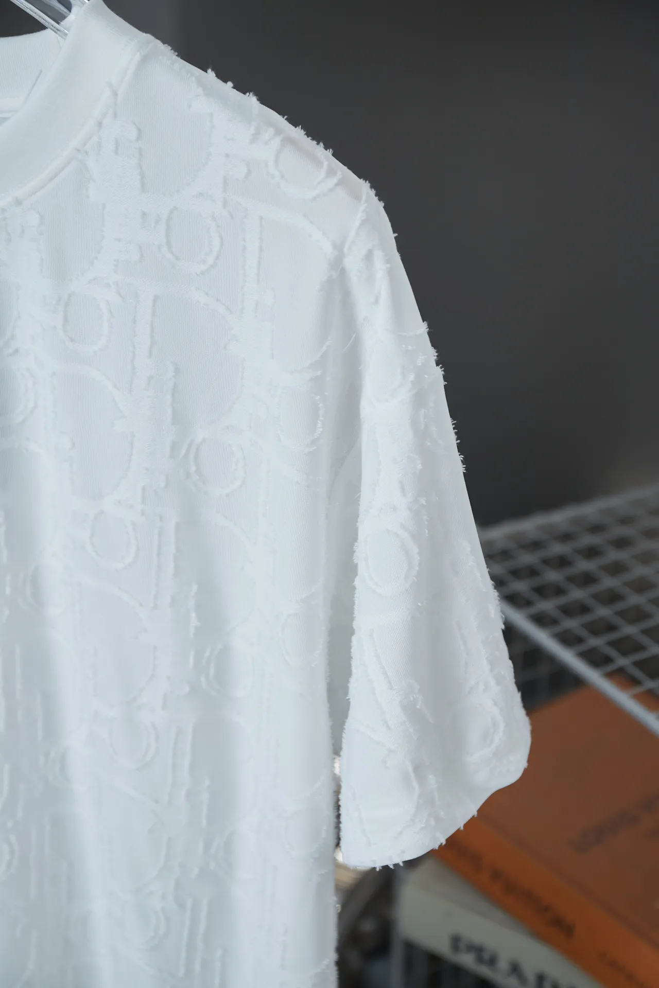 🅿️180 Dior 2025 new style embossed jacquard short-sleeved pure cotton plain fabric, woven with 32S double-strand pure cotton yarn. The 32S double-strand is twisted from two 32-count single yarns. The yarn is thicker and stronger. The fabric has high wear resistance while retaining the moisture absorption and breathability of pure cotton. The plain weave has a tight structure and a smooth surface, but it feels relatively stiff and supports the stiffness of the pattern. The jacquard pattern uses thread-cutting jacquard technology, and the full-width Oblique jacquard pattern forms a relief effect through the deep integration of full-width jacquard and shearing technology. The jacquard structure provides a three-dimensional frame, and the shearing process enhances local texture. The electronic jacquard machine is used to weave complex patterns on the entire fabric to form a three-dimensional concave and convex texture, achieving the integration of texture and pattern. The raised jacquard is cut in a directional manner to create a relief effect, enhancing tactile layering and visual contrast. Straight crew neck fit. Cut and sewn in floral position, standard H hanging fit, with shoulder-length design. The vertical version emphasizes that the width of the shoulders, waist, and hem are basically the same, and it is simple and loose. The short sleeves are tailored to fit the body of the wearer. At the same time, the neckline, cuffs and hem of the short sleeves are all designed with double lines. S M L XL
