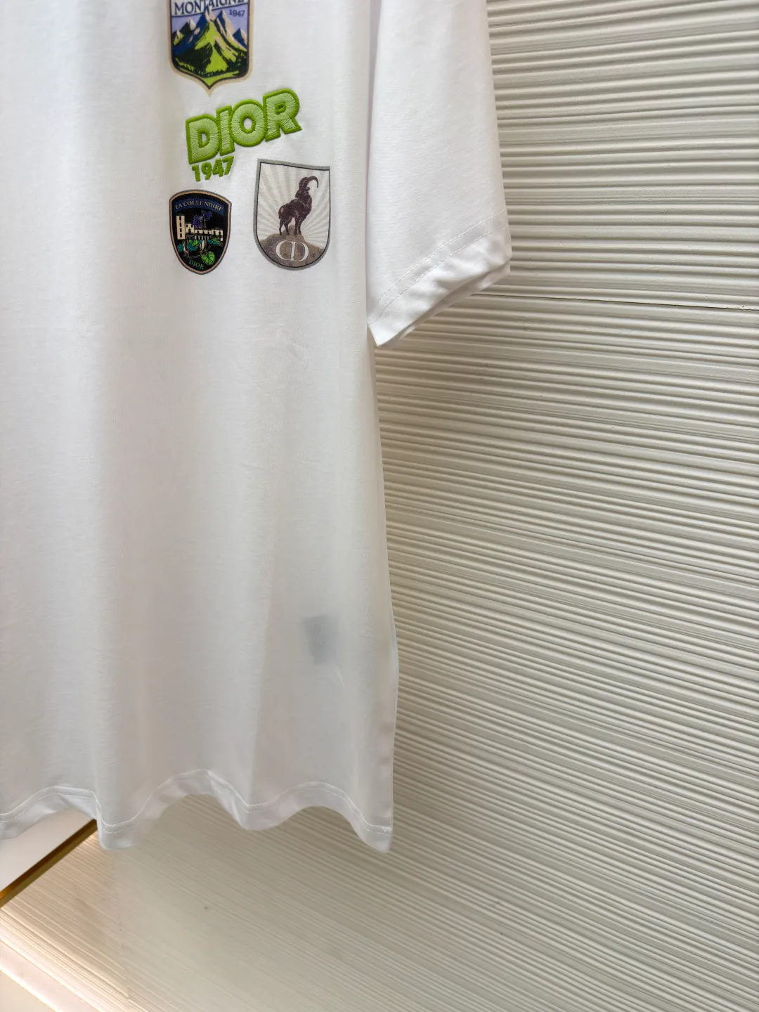 Dior Alpine Embroidery Round Neck Short Sleeve ●Original version: Purchased and developed by 7149 ●Item number: 1681102-A05 ●Fabric: plain knitted fabric ●Technology: White ink direct injection production ●Version: Fitted version ●Weight: about 200 grams ●Size: XS-S-M-L ●Description: The main body is made of 24S special woven compact cotton to make plain knitted fabric, weight 180g. High-count combed cotton yarn eliminates most of the short hairiness through compact spinning process, making the yarn smoother and stronger. The woven fabric structure is extremely dense, flat and soft, with excellent anti-pilling ability and durability, while retaining the natural advantages of pure cotton, which is breathable and skin-friendly. The neckline is made of 32S 1x1 rib with a weight of 300g. The finer yarn count creates a more delicate and tight thread, which provides better elasticity and deformation resistance than ordinary ribs, ensuring that the neckline can still remain stiff after being put on and taken off many times. The printed pattern and classic logo inspired by the mountain spirit on the chest become the visual focus through the decoration combined with multiple techniques. The printed pattern elements use digital white ink direct injection technology, which presents bright, opaque white and color patterns on dark fabrics with clear edges and a smooth touch. The classic logo is completed with fluorescent green contrasting letters in the form of patches, which are then precisely sewn onto the fabric using appliqué technology. This process restores the three-dimensionality, color saturation and detail accuracy of the pattern to the original version. With the standard round neck shape and basic color, this product has established a high degree of matching tolerance. It can be mixed and matched with daily jeans or shorts, catering to the pursuit of functionality, comfort and details. The neckline has a rounded arc, suitable for various face shapes and body shapes; the sleeves are moderate and end just above the elbow, showing a smart and neat image. The slim-fitting cut shows off the wearer's body curves without sacrificing comfort. The collar, cuffs, hem and other parts are all sewn with fine double-needle stitching. The overall wiring is straight and delicate, the fabric is comfortable and soft, and the color is consistent without color difference. It can be matched with the same style to create a fashionable look and control various occasions. Customized accessories, complete with three standards, same style for men and women!