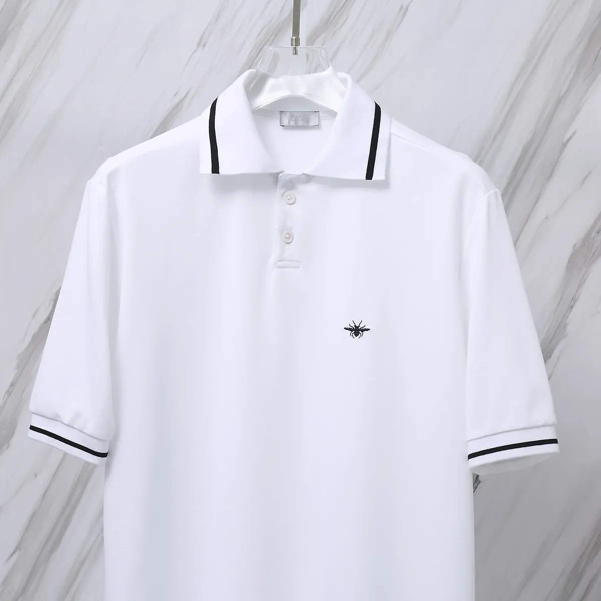 🅿️190 Item No. D41 (Dior classic little bee logo embroidered POLO shirt) Dior Dior 24ss new little bee letter embroidered logo lapel polo shirt short-sleeved T-shirt. The counter restores the top replica for men and women. The own factory style is very good, business commuting, classic POLO lapel design, classic small logo embroidery design on the chest highlights personality, making the entire line smoother, the most classic evergreen small logo design Exquisite embroidered logo design on the chest, pure cotton texture that is skin-friendly and comfortable. Suitable for both business and leisure. The piqué cotton fabric is more breathable and dry than ordinary knitted fabrics. 3D three-dimensional tailoring technology, the upper body is three-dimensional. The embroidery on the chest is full of details, and the embroidery with thousands of needles is three-dimensional and full. It is made of 240 grams of pure cotton piqué fabric and customized buttons. Top quality product. Color: White Size: S/M/L/XL