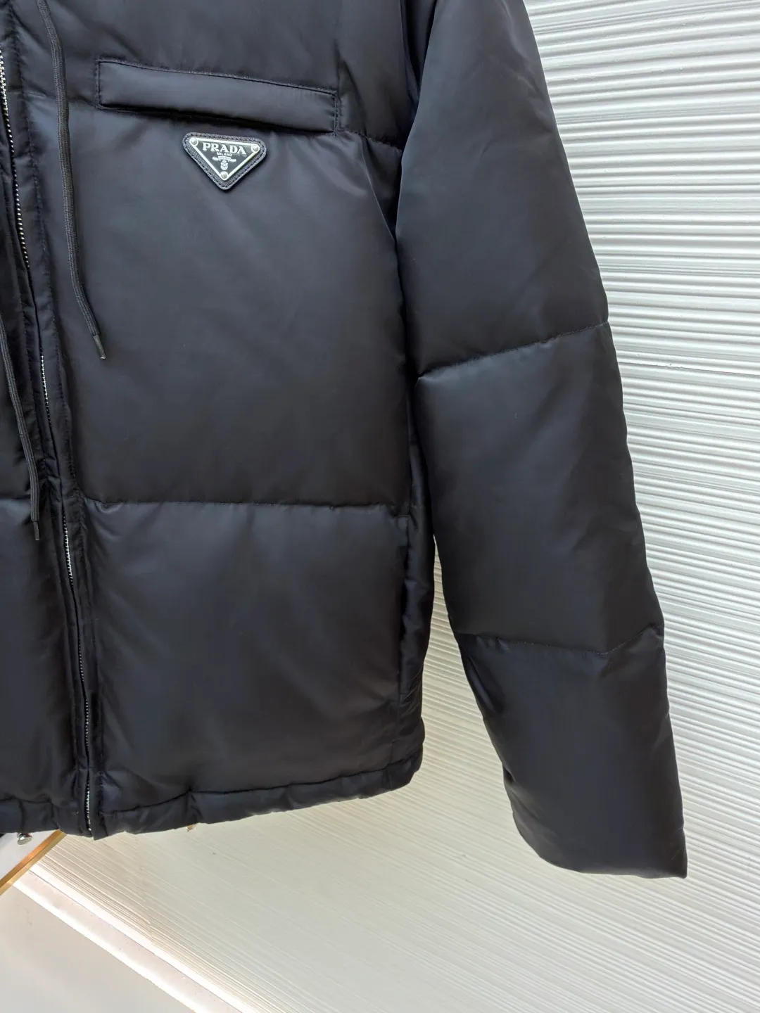 Prada Triangle Down Jacket ●Item No.: 1681316-C75 ●Fabric: White duck down fabric ●Technology: Mechanically filled with down ●Color: Black ●Version: Fitted version ●Weight: about 910 grams ●Size: S-M-L-XL ●Description: This down jacket is made of high-density water-repellent fabric, treated with a special coating, and has both windproof and anti-fouling properties. The hooded design is equipped with an adjustable drawstring, and the metal buckle at the end of the drawstring is customized by the brand, with fine texture and durability. The placket uses a two-way metal zipper with precise teeth, and the smoothness of the zipper has been tested for many rounds. The body of the garment is filled with high-quality goose down, which is evenly and plumply filled. The velvet is fixed through three-dimensional quilting technology to avoid velvet running while creating a layered silhouette. The brand triangle logo on the chest uses metal embossing + leather inlay technology, the edges are polished smooth, and the logo is three-dimensional and eye-catching. The pocket is a hidden zipper bag, and the zipper is the same color as the fabric, which is both practical and beautiful. The cuffs use micro-elastic edge processing to fit the wrist without restricting movement. The overall tailoring follows an oversize version, and seamless gluing technology is used at the splicing points to reduce thread exposure and improve wearing comfort and sophistication of garments. Every craftsmanship demonstrates Prada's strict standards for high-end clothing. The overall wiring is straight and delicate, the fabric is comfortable and soft, and the color is consistent without color difference. It can be matched with the same style to create a fashionable look and control various occasions. Customized accessories, complete with three standards, same style for men and women!