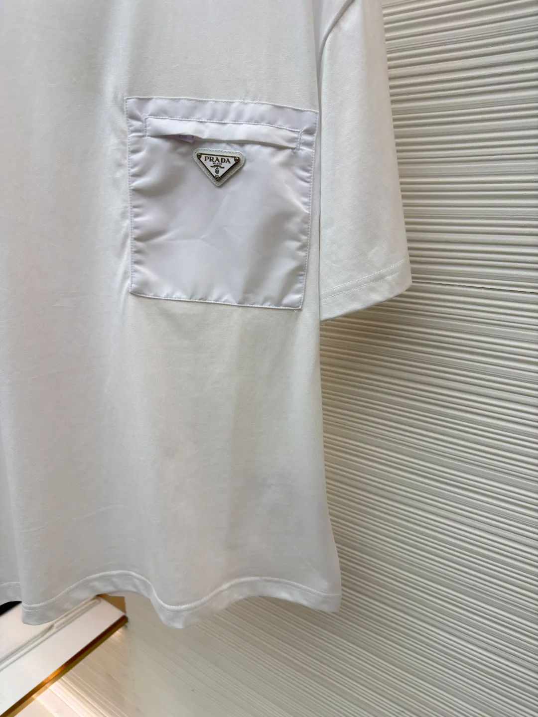 Prada Triangle Logo Pocket Short Sleeves ●Original version: Purchased and developed for 7000 ●Item number: 1682395-A05 ●Fabric: High-elastic jersey fabric ●Technology: Needle and shuttle splicing ●Color: white ●Version: Fitted version ●Weight: about 230 grams ●Size: S-M-L-XL ●Description: Customized high-elastic jersey material, delicate and soft, comfortable and close to the skin, a touch of simple white, as pure as ever, elegant and self-evident The iconic Prada triangle logo is embellished on the chest. It is integrated with Re-Nylon nylon fabric to decorate the square silhouette. Cross-disciplinary aesthetic grafting. The exquisite small pocket design highlights quality and style. It reveals a flexible and relaxed beauty. It is a picture of strolling in the city and deconstructs the attitude of the modern gentleman. The infrared positioning of the "Prada triangle mark" by an imported special machine is more precise and firm. Needle and shuttle stitching technology can make full use of the respective advantages of knitted fabrics and woven fabrics. By choosing the appropriate sewing process and stitches, it can ensure that the splicing parts are strong and beautiful. Template machine bag opening The preset template guides the position, shape and size of the bag opening. The accuracy ensures the quality of the bag opening effect. The overall wiring is straight and delicate, the fabric is comfortable and soft, and the color is consistent without color difference. It can be matched with the same style to create a fashionable look and control various occasions. Customized accessories, complete with three standards, same style for men and women!