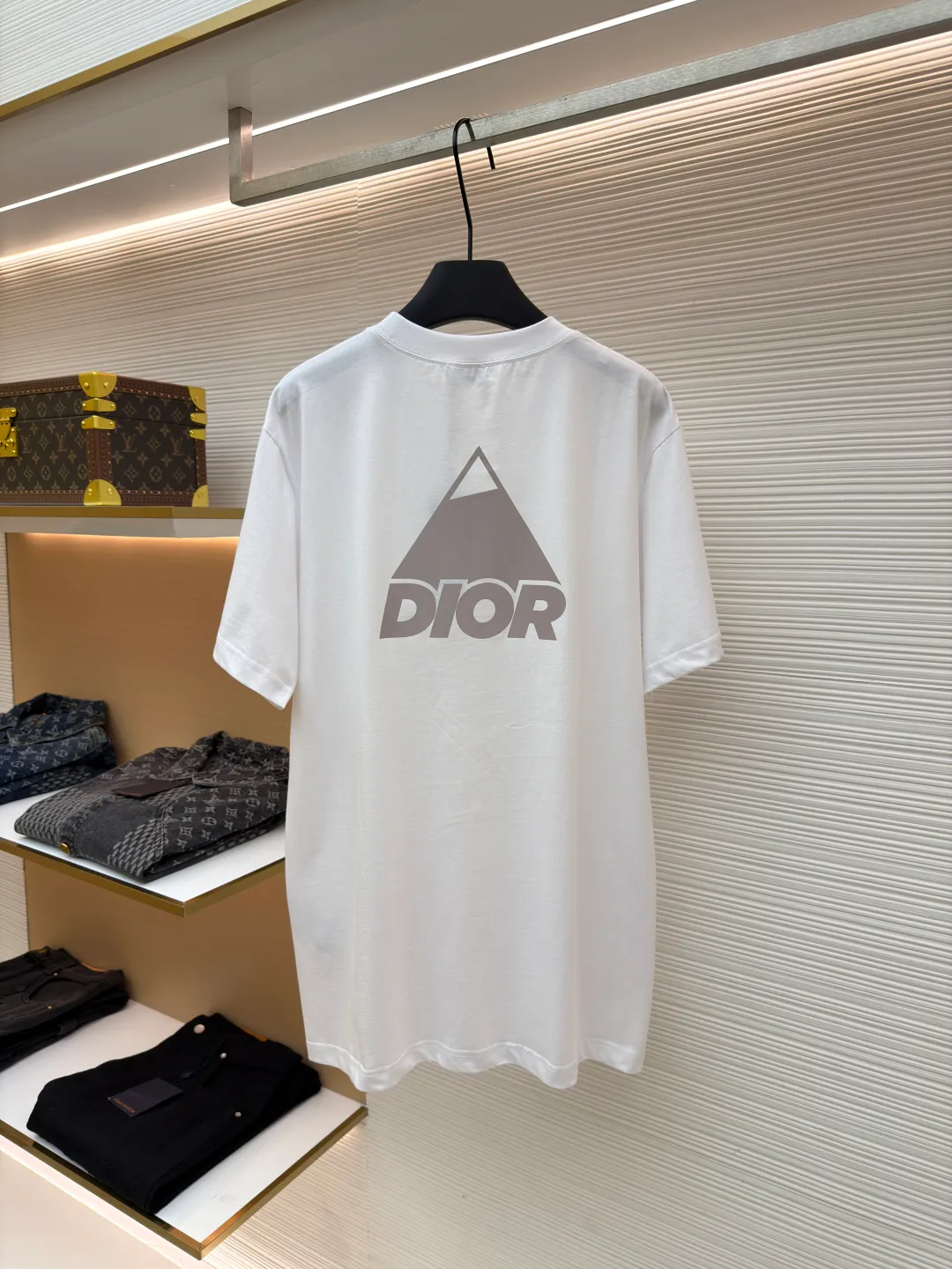 Dior Reflective Triangle Icon Round Neck Short Sleeve ●Item No.: 1681100-A00 ●Fabric: Jersey fabric ●Technology: Reflective lettering and embossed production ●Version: Fitted version ●Weight: about 205 grams ●Size: S-M-L-XL ●Description: The main body is made of 24S special woven compact cotton to make jersey fabric, weight 180g. High-count combed cotton yarn eliminates most of the short hairiness through compact spinning process, making the yarn smoother and stronger. The woven fabric structure is extremely dense, flat and soft, with excellent anti-pilling ability and durability, while retaining the natural advantages of pure cotton, which is breathable and skin-friendly. The neckline is made of 32S 1x1 rib with a weight of 300g. The finer yarn count creates a more delicate and tight thread, which provides better elasticity and deformation resistance than ordinary ribs, ensuring that the neckline can still remain stiff after being put on and taken off many times. The reflective engraving and embossing process is a sophisticated technology that combines safety functions with visual aesthetics. The core is to use a reflective lettering film with a built-in micro-glass bead layer. First, a high-precision laser cutting machine is used to engrave the outline according to the designed fonts and patterns to ensure that the edges are clear and burr-free. The cut reflective film is accurately attached to the surface of the fabric through heat transfer printing equipment under specific temperature and pressure, so that it is firmly combined with the fabric fibers. The case is matte silver-gray under normal conditions, but when illuminated by light, the micro-glass bead layer can achieve efficient retroreflection and instantly present a striking bright effect. The finished product is washable and abrasion resistant, perfectly meeting the dual needs of sportswear for functionality and visual tension. The overall wiring is straight and delicate, the fabric is comfortable and soft, and the color is consistent without color difference. It can be matched with the same style to create a fashionable look and control various occasions. Customized accessories, complete with three standards, same style for men and women!