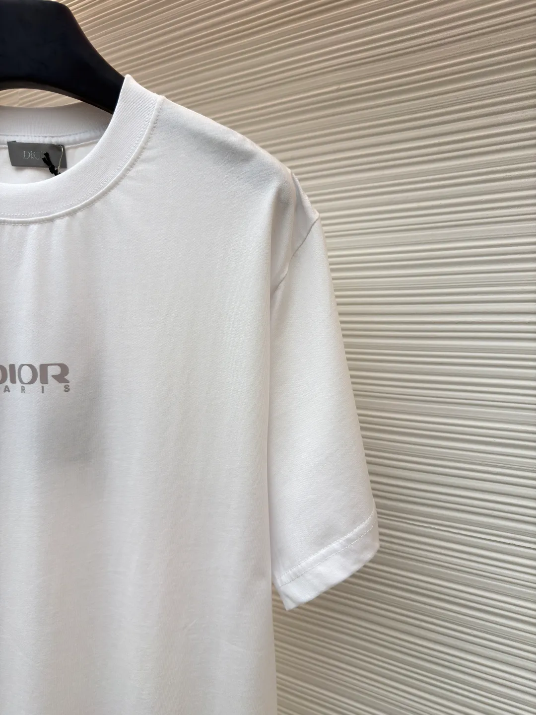 Dior Reflective Triangle Icon Round Neck Short Sleeve ●Item No.: 1681100-A00 ●Fabric: Jersey fabric ●Technology: Reflective lettering and embossed production ●Version: Fitted version ●Weight: about 205 grams ●Size: S-M-L-XL ●Description: The main body is made of 24S special woven compact cotton to make jersey fabric, weight 180g. High-count combed cotton yarn eliminates most of the short hairiness through compact spinning process, making the yarn smoother and stronger. The woven fabric structure is extremely dense, flat and soft, with excellent anti-pilling ability and durability, while retaining the natural advantages of pure cotton, which is breathable and skin-friendly. The neckline is made of 32S 1x1 rib with a weight of 300g. The finer yarn count creates a more delicate and tight thread, which provides better elasticity and deformation resistance than ordinary ribs, ensuring that the neckline can still remain stiff after being put on and taken off many times. The reflective engraving and embossing process is a sophisticated technology that combines safety functions with visual aesthetics. The core is to use a reflective lettering film with a built-in micro-glass bead layer. First, a high-precision laser cutting machine is used to engrave the outline according to the designed fonts and patterns to ensure that the edges are clear and burr-free. The cut reflective film is accurately attached to the surface of the fabric through heat transfer printing equipment under specific temperature and pressure, so that it is firmly combined with the fabric fibers. The case is matte silver-gray under normal conditions, but when illuminated by light, the micro-glass bead layer can achieve efficient retroreflection and instantly present a striking bright effect. The finished product is washable and abrasion resistant, perfectly meeting the dual needs of sportswear for functionality and visual tension. The overall wiring is straight and delicate, the fabric is comfortable and soft, and the color is consistent without color difference. It can be matched with the same style to create a fashionable look and control various occasions. Customized accessories, complete with three standards, same style for men and women!