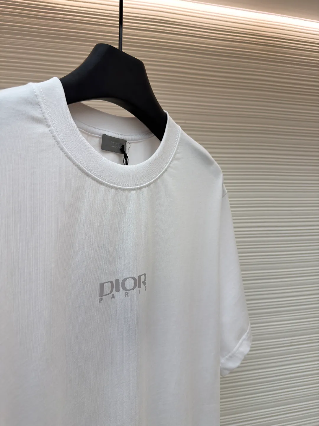 Dior Reflective Triangle Icon Round Neck Short Sleeve ●Item No.: 1681100-A00 ●Fabric: Jersey fabric ●Technology: Reflective lettering and embossed production ●Version: Fitted version ●Weight: about 205 grams ●Size: S-M-L-XL ●Description: The main body is made of 24S special woven compact cotton to make jersey fabric, weight 180g. High-count combed cotton yarn eliminates most of the short hairiness through compact spinning process, making the yarn smoother and stronger. The woven fabric structure is extremely dense, flat and soft, with excellent anti-pilling ability and durability, while retaining the natural advantages of pure cotton, which is breathable and skin-friendly. The neckline is made of 32S 1x1 rib with a weight of 300g. The finer yarn count creates a more delicate and tight thread, which provides better elasticity and deformation resistance than ordinary ribs, ensuring that the neckline can still remain stiff after being put on and taken off many times. The reflective engraving and embossing process is a sophisticated technology that combines safety functions with visual aesthetics. The core is to use a reflective lettering film with a built-in micro-glass bead layer. First, a high-precision laser cutting machine is used to engrave the outline according to the designed fonts and patterns to ensure that the edges are clear and burr-free. The cut reflective film is accurately attached to the surface of the fabric through heat transfer printing equipment under specific temperature and pressure, so that it is firmly combined with the fabric fibers. The case is matte silver-gray under normal conditions, but when illuminated by light, the micro-glass bead layer can achieve efficient retroreflection and instantly present a striking bright effect. The finished product is washable and abrasion resistant, perfectly meeting the dual needs of sportswear for functionality and visual tension. The overall wiring is straight and delicate, the fabric is comfortable and soft, and the color is consistent without color difference. It can be matched with the same style to create a fashionable look and control various occasions. Customized accessories, complete with three standards, same style for men and women!