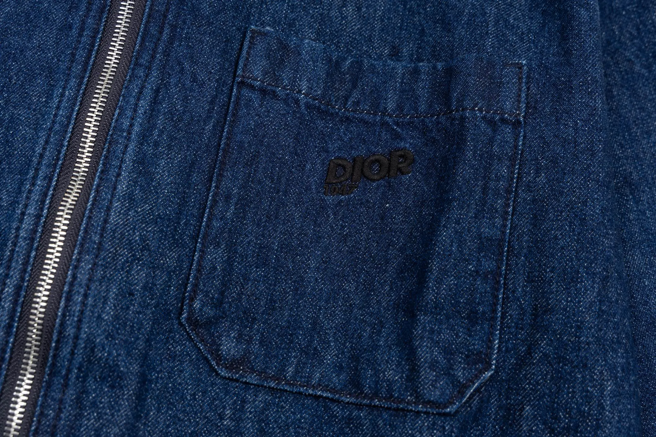 🅿️600 CD 26SS 1947 letter embroidered denim jacket. This jacket shirt is a new product of the 2026 spring men's wear series. It is decorated with multi-color patches, showing the alpine spirit and the classic logo of high-end style inspired by CD archives. Crafted from blue cotton denim for a lightweight feel, it features embroidery on the chest pocket and back. It features a front zipper closure and can be paired with the matching jeans for a sophisticated look. Using high-count cotton denim, through weight reduction textile technology and special washing treatment, while retaining the twill texture and denim durability, the fabric weight has been successfully reduced to the ideal state. The finished product has a cloud-like soft and waxy feel and excellent drape, which subverts the heavy impression of denim. The three-dimensional layering is created through patch pocket technology with a strong hand-feel, and delicate letter outlines are constructed on the chest and back using contrasting embroidery threads and three-dimensional embroidery techniques. The stitch density has been carefully calculated to ensure that the pattern still maintains a high-definition level of clarity despite the rough texture of the denim. The overall structure adopts a jacket-like shirt structure, with precision toothed chain and pull tab design as the opening and closing design, taking into account smooth operation experience and windproof performance. Functional details such as chest patch pockets inside and outside continue the pragmatic logic, and all seam interfaces are secondary reinforced to meet the durability needs of outdoor scenes while maintaining the contours. Size:44-46-48-50