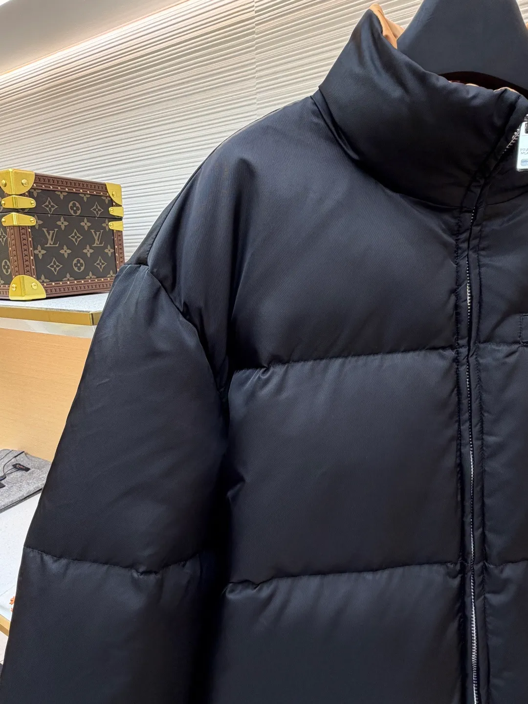 Prada logo stand collar down jacket ●Item number: 1681794-C75 ●Material: white duck down fabric ●Technology: mechanical down filling ●Color: black ●Version: fitted version ●Weight: about 855 grams ●Size: S-M-L-XL ●Description: The recycled nylon fabric made of 100% nylon is woven into a tight and tough fabric through advanced textile technology. The strength of the frame is increased to effectively block the invasion of cold wind and lock the warm air generated by the down layer. After a tight weaving process and special treatment, it is waterproof and windproof. The surface forms a certain lotus leaf effect. It is also anti-wrinkle and not easy to deform, making it easy for daily care. The inner lining is made of caramel brown nylon fabric woven from 100% polyamide. When folded, it creates a strong color contrast, just like the molten gold of the setting sun pouring into the deep night sky. Polyamide fiber is known for its extremely high strength and excellent skin-friendly feel. It feels silky smooth and avoids the friction and discomfort that may occur when wearing heavy underwear. It works together with the outer layer of nylon to create a breathable, temperature-locking, and extremely comfortable microclimate environment, allowing warmth and care to be online at all times without feeling stuffy or restrictive. It uses 90 white duck down with a fill power of 220g to ensure excellent thermal insulation performance. After the velvet has been strictly screened and processed, it is not easy to drill. The 6cm tall stand-up collar fits the neck line without being oppressive, and is as warm as a "second skin" in the cold wind. The junction between the collar and the zipper adopts a bevel splicing process to avoid the rigid feeling of traditional stand-up collars and make it more flexible when you turn your head. The hem has built-in metal adjustment buckles on both sides. You can gently pull it down to tighten the waistline, and lift it up to restore the loose silhouette - it is neat and slim when commuting, and it is free and unrestrained when outdoors. The metal surface of the adjustment buckle is treated with PVD coating, which is wear-resistant and corrosion-resistant, and will last forever. The overall wiring is straight and delicate, the fabric is comfortable and soft, and the color is consistent without color difference. It can be matched with the same style to create a fashionable look and control various occasions. Customized accessories, complete with three standards, same style for men and women!