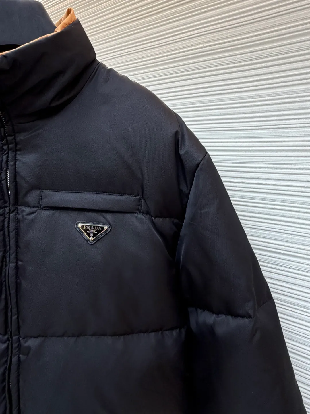 Prada logo stand collar down jacket ●Item number: 1681794-C75 ●Material: white duck down fabric ●Technology: mechanical down filling ●Color: black ●Version: fitted version ●Weight: about 855 grams ●Size: S-M-L-XL ●Description: The recycled nylon fabric made of 100% nylon is woven into a tight and tough fabric through advanced textile technology. The strength of the frame is increased to effectively block the invasion of cold wind and lock the warm air generated by the down layer. After a tight weaving process and special treatment, it is waterproof and windproof. The surface forms a certain lotus leaf effect. It is also anti-wrinkle and not easy to deform, making it easy for daily care. The inner lining is made of caramel brown nylon fabric woven from 100% polyamide. When folded, it creates a strong color contrast, just like the molten gold of the setting sun pouring into the deep night sky. Polyamide fiber is known for its extremely high strength and excellent skin-friendly feel. It feels silky smooth and avoids the friction and discomfort that may occur when wearing heavy underwear. It works together with the outer layer of nylon to create a breathable, temperature-locking, and extremely comfortable microclimate environment, allowing warmth and care to be online at all times without feeling stuffy or restrictive. It uses 90 white duck down with a fill power of 220g to ensure excellent thermal insulation performance. After the velvet has been strictly screened and processed, it is not easy to drill. The 6cm tall stand-up collar fits the neck line without being oppressive, and is as warm as a "second skin" in the cold wind. The junction between the collar and the zipper adopts a bevel splicing process to avoid the rigid feeling of traditional stand-up collars and make it more flexible when you turn your head. The hem has built-in metal adjustment buckles on both sides. You can gently pull it down to tighten the waistline, and lift it up to restore the loose silhouette - it is neat and slim when commuting, and it is free and unrestrained when outdoors. The metal surface of the adjustment buckle is treated with PVD coating, which is wear-resistant and corrosion-resistant, and will last forever. The overall wiring is straight and delicate, the fabric is comfortable and soft, and the color is consistent without color difference. It can be matched with the same style to create a fashionable look and control various occasions. Customized accessories, complete with three standards, same style for men and women!