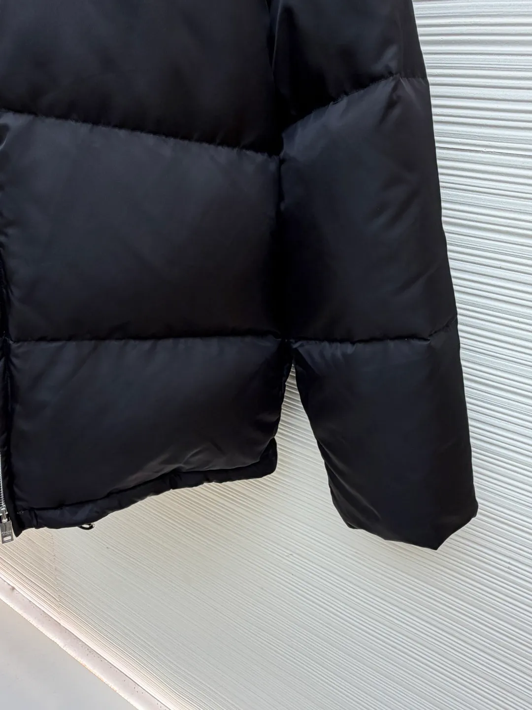 Prada logo stand collar down jacket ●Item number: 1681794-C75 ●Material: white duck down fabric ●Technology: mechanical down filling ●Color: black ●Version: fitted version ●Weight: about 855 grams ●Size: S-M-L-XL ●Description: The recycled nylon fabric made of 100% nylon is woven into a tight and tough fabric through advanced textile technology. The strength of the frame is increased to effectively block the invasion of cold wind and lock the warm air generated by the down layer. After a tight weaving process and special treatment, it is waterproof and windproof. The surface forms a certain lotus leaf effect. It is also anti-wrinkle and not easy to deform, making it easy for daily care. The inner lining is made of caramel brown nylon fabric woven from 100% polyamide. When folded, it creates a strong color contrast, just like the molten gold of the setting sun pouring into the deep night sky. Polyamide fiber is known for its extremely high strength and excellent skin-friendly feel. It feels silky smooth and avoids the friction and discomfort that may occur when wearing heavy underwear. It works together with the outer layer of nylon to create a breathable, temperature-locking, and extremely comfortable microclimate environment, allowing warmth and care to be online at all times without feeling stuffy or restrictive. It uses 90 white duck down with a fill power of 220g to ensure excellent thermal insulation performance. After the velvet has been strictly screened and processed, it is not easy to drill. The 6cm tall stand-up collar fits the neck line without being oppressive, and is as warm as a "second skin" in the cold wind. The junction between the collar and the zipper adopts a bevel splicing process to avoid the rigid feeling of traditional stand-up collars and make it more flexible when you turn your head. The hem has built-in metal adjustment buckles on both sides. You can gently pull it down to tighten the waistline, and lift it up to restore the loose silhouette - it is neat and slim when commuting, and it is free and unrestrained when outdoors. The metal surface of the adjustment buckle is treated with PVD coating, which is wear-resistant and corrosion-resistant, and will last forever. The overall wiring is straight and delicate, the fabric is comfortable and soft, and the color is consistent without color difference. It can be matched with the same style to create a fashionable look and control various occasions. Customized accessories, complete with three standards, same style for men and women!