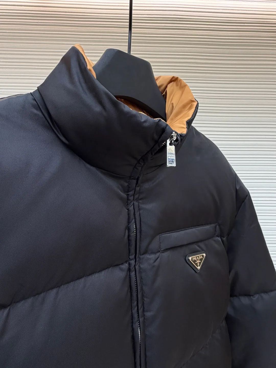 Prada logo stand collar down jacket ●Item number: 1681794-C75 ●Material: white duck down fabric ●Technology: mechanical down filling ●Color: black ●Version: fitted version ●Weight: about 855 grams ●Size: S-M-L-XL ●Description: The recycled nylon fabric made of 100% nylon is woven into a tight and tough fabric through advanced textile technology. The strength of the frame is increased to effectively block the invasion of cold wind and lock the warm air generated by the down layer. After a tight weaving process and special treatment, it is waterproof and windproof. The surface forms a certain lotus leaf effect. It is also anti-wrinkle and not easy to deform, making it easy for daily care. The inner lining is made of caramel brown nylon fabric woven from 100% polyamide. When folded, it creates a strong color contrast, just like the molten gold of the setting sun pouring into the deep night sky. Polyamide fiber is known for its extremely high strength and excellent skin-friendly feel. It feels silky smooth and avoids the friction and discomfort that may occur when wearing heavy underwear. It works together with the outer layer of nylon to create a breathable, temperature-locking, and extremely comfortable microclimate environment, allowing warmth and care to be online at all times without feeling stuffy or restrictive. It uses 90 white duck down with a fill power of 220g to ensure excellent thermal insulation performance. After the velvet has been strictly screened and processed, it is not easy to drill. The 6cm tall stand-up collar fits the neck line without being oppressive, and is as warm as a "second skin" in the cold wind. The junction between the collar and the zipper adopts a bevel splicing process to avoid the rigid feeling of traditional stand-up collars and make it more flexible when you turn your head. The hem has built-in metal adjustment buckles on both sides. You can gently pull it down to tighten the waistline, and lift it up to restore the loose silhouette - it is neat and slim when commuting, and it is free and unrestrained when outdoors. The metal surface of the adjustment buckle is treated with PVD coating, which is wear-resistant and corrosion-resistant, and will last forever. The overall wiring is straight and delicate, the fabric is comfortable and soft, and the color is consistent without color difference. It can be matched with the same style to create a fashionable look and control various occasions. Customized accessories, complete with three standards, same style for men and women!