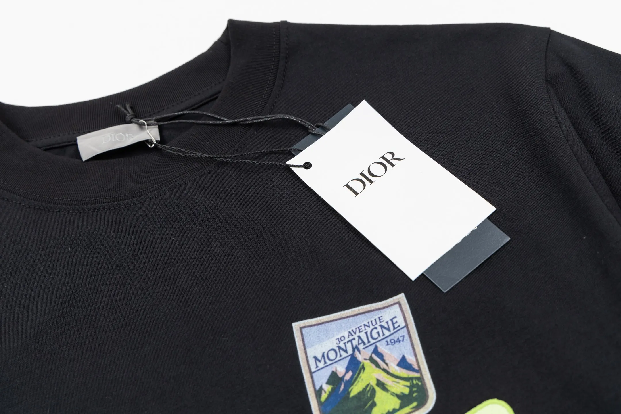 🅿️280 CD Mountain Alpine Shield Print Short Sleeve (Black) The fabric is made of 24S 185g special woven compact cotton fabric, and the rib is made of 32S 300g double yarn rib. This Mountain T-shirt is a new product of the 2026 spring men's wear series. It is decorated with multi-color patches to show the mountain spirit and the classic logo of high-end style inspired by archives. Crafted from white cotton jersey, it features a crew neck for a refined look. The fabric is made of 24S special-spun compact cotton as a plain knitted base. The high-count compact spinning process ensures that the fabric has an extremely delicate skin feel and excellent anti-pilling durability. The neckline is equipped with 32S 1x1 high-density ribbing, which provides long-lasting rebound with its tight structure and protects the collar shape. The decorative multi-color embroidery patch adopts appliqué technique. Three-dimensional lines and fluorescent details are first embroidered with high-density stitches on independent fabrics, and then accurately covered on the chest, forming a strong visual hierarchy and tactile contrast. The alpine element pattern uses digital white ink direct injection technology, with saturated colors and sharp edges, which together with the embroidery patch create a rich texture. Size:XS-S-M-L