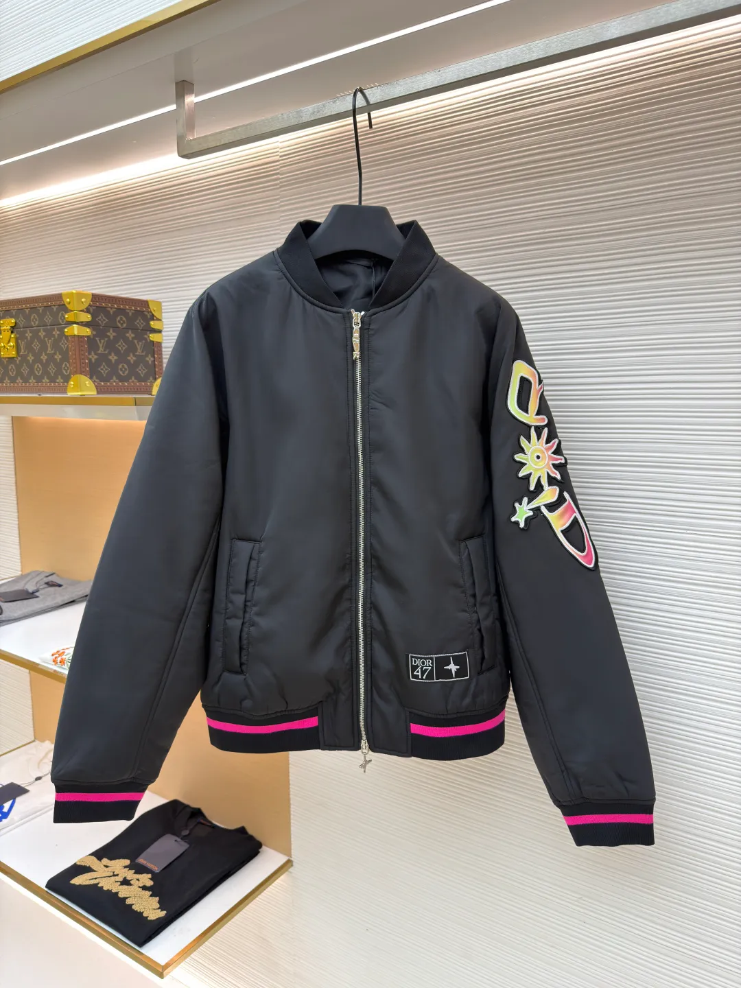 Dior Hamilton joint baseball uniform ●Original version: 32000 purchased and developed ●Item number: 1681336-B90 ●Fabric: nylon fabric ●Technology: printing production ●Color: black ●Version: fitted version ●Weight: about 830 grams ●Size: 48-50-52-54 ●Description: Made of high-quality matte nylon fabric, the texture is stiff and windproof. It has been treated with a special coating to improve wear resistance and texture, and provide good shape support for the jacket. The colorful letter pattern on the sleeves uses a multi-layer offset printing process, with natural color gradients and strong adhesion; the "DIOR 47" logo on the chest is precision embroidered, with fine stitching and high integration with the fabric, highlighting the brand's craftsmanship. Made from a classic baseball uniform cut, the silhouette is sleek and stylish. Double thread reinforcement is used during sewing, the seams are smooth and snug, the stitch spacing is even, and the lines are straight, reflecting the rigorous garment making process. The zipper is a brand-customized metal zipper with brand details on the zipper puller, which is smooth and durable; the ribbed collar, cuffs and hem are made of high-elastic knitting technology, which has good elasticity, is comfortable to wear and can effectively prevent wind. The pockets on both sides are designed as hidden pockets, which are practical while maintaining overall beauty; the pink trim on the body contrasts sharply with the main black tone, and the craftsmanship details reflect the brand's high-end production standards.