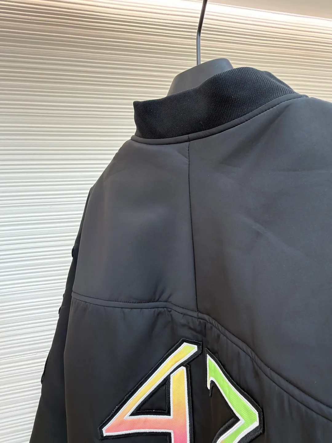 Dior Hamilton joint baseball uniform ●Original version: 32000 purchased and developed ●Item number: 1681336-B90 ●Fabric: nylon fabric ●Technology: printing production ●Color: black ●Version: fitted version ●Weight: about 830 grams ●Size: 48-50-52-54 ●Description: Made of high-quality matte nylon fabric, the texture is stiff and windproof. It has been treated with a special coating to improve wear resistance and texture, and provide good shape support for the jacket. The colorful letter pattern on the sleeves uses a multi-layer offset printing process, with natural color gradients and strong adhesion; the "DIOR 47" logo on the chest is precision embroidered, with fine stitching and high integration with the fabric, highlighting the brand's craftsmanship. Made from a classic baseball uniform cut, the silhouette is sleek and stylish. Double thread reinforcement is used during sewing, the seams are smooth and snug, the stitch spacing is even, and the lines are straight, reflecting the rigorous garment making process. The zipper is a brand-customized metal zipper with brand details on the zipper puller, which is smooth and durable; the ribbed collar, cuffs and hem are made of high-elastic knitting technology, which has good elasticity, is comfortable to wear and can effectively prevent wind. The pockets on both sides are designed as hidden pockets, which are practical while maintaining overall beauty; the pink trim on the body contrasts sharply with the main black tone, and the craftsmanship details reflect the brand's high-end production standards.