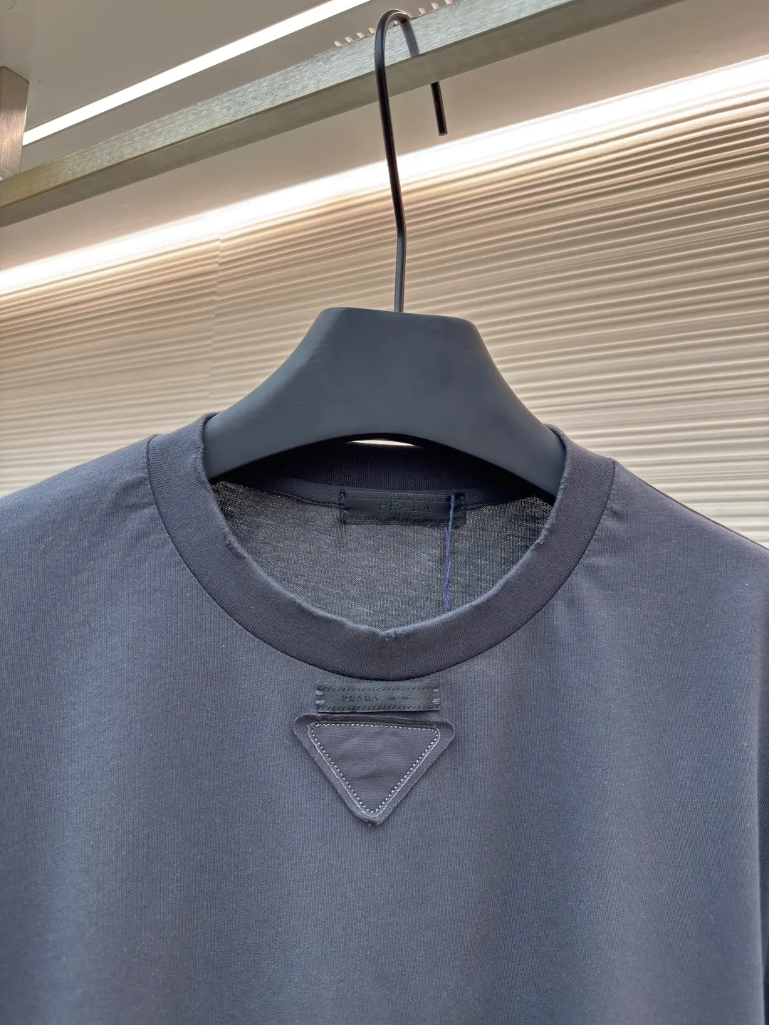 Prada Pencil Gray Long Sleeve ●Original version: Purchased and developed by 8934 ●Item number: 1680720-A05 ●Fabric: combed plain weave fabric ●Technology: Laser burning ●Version: fitted version ●Weight: about 240 grams ●Size: S-M-L-XL ●Description: Custom-woven 50S 190G combed plain weave fabric, non-market general gray fabric, needs to be fully customized from yarn ratio and loom parameters. Short fiber impurities are removed through the combing process to ensure that the yarn is longer and more uniform, and the fabric surface is smooth and hairless.  Specially dyed pencil gray, the color is adjusted individually instead of using a standard color card. Multiple proofing is required to match the low saturation gray tone specified by Prada. Chest triangle laser burnt embroidery shaping: Laser burnt: high-precision laser engraving, carbonizing the fabric surface to form a gradient etching texture, and the edges need to be manually adjusted to avoid scorch marks.  Composite embroidery: superimpose embroidery on the basis of burnt flowers. The stitch density needs to be aligned with the burnt flowers pattern to prevent fabric deformation.  Three-dimensional shaping: Use high-temperature pressing or resin coating to maintain the relief of the triangular structure and avoid collapse after washing. The overall wiring is straight and delicate, the fabric is comfortable and soft, and the color is consistent without color difference. It can be matched with the same style to create a fashionable look and control various occasions. Customized accessories, complete with three standards, same style for men and women!