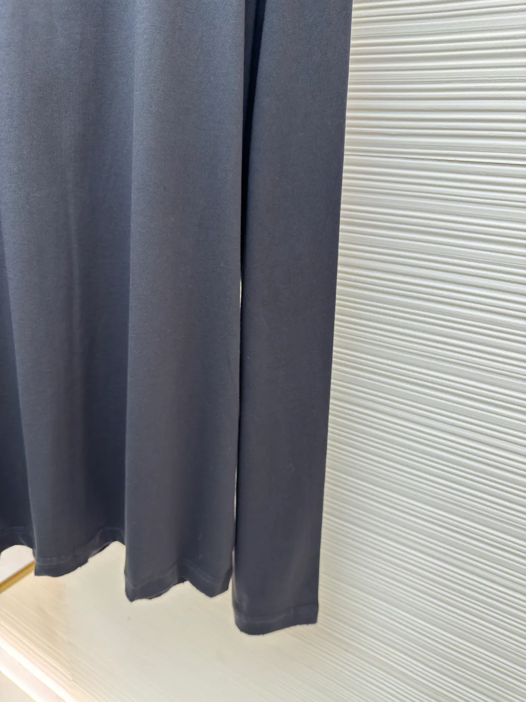 Prada Pencil Gray Long Sleeve ●Original version: Purchased and developed by 8934 ●Item number: 1680720-A05 ●Fabric: combed plain weave fabric ●Technology: Laser burning ●Version: fitted version ●Weight: about 240 grams ●Size: S-M-L-XL ●Description: Custom-woven 50S 190G combed plain weave fabric, non-market general gray fabric, needs to be fully customized from yarn ratio and loom parameters. Short fiber impurities are removed through the combing process to ensure that the yarn is longer and more uniform, and the fabric surface is smooth and hairless.  Specially dyed pencil gray, the color is adjusted individually instead of using a standard color card. Multiple proofing is required to match the low saturation gray tone specified by Prada. Chest triangle laser burnt embroidery shaping: Laser burnt: high-precision laser engraving, carbonizing the fabric surface to form a gradient etching texture, and the edges need to be manually adjusted to avoid scorch marks.  Composite embroidery: superimpose embroidery on the basis of burnt flowers. The stitch density needs to be aligned with the burnt flowers pattern to prevent fabric deformation.  Three-dimensional shaping: Use high-temperature pressing or resin coating to maintain the relief of the triangular structure and avoid collapse after washing. The overall wiring is straight and delicate, the fabric is comfortable and soft, and the color is consistent without color difference. It can be matched with the same style to create a fashionable look and control various occasions. Customized accessories, complete with three standards, same style for men and women!