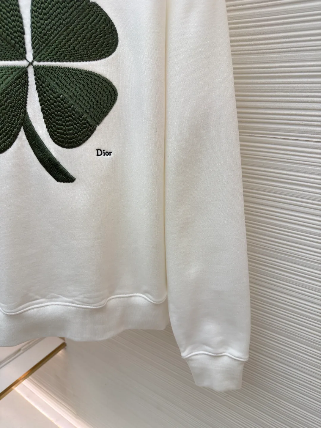 Dior four-leaf clover round neck sweatshirt ●Original version: purchased and developed by 19189 ●Item number: 1682447-A55 ●Material: pure cotton terry bottom sweatshirt fabric ●Technology: hollow embroidery production of coarse wool yarn ●Color: white ●Version: fitted version ●Weight: about 565 grams ●Size: XS-S-M-L ●Description: It adopts a fleece fabric structure of 26-count double yarn surface + 10-count yarn bottom, with a weight of 380g/㎡; with the same weight of 21-count 1x1 rib 470g/㎡. The 26-count double yarn forms a smooth and dense outer surface, and the 10-count yarn base is precisely brushed to form a rich and uniform velvet layer, thereby simultaneously achieving a crisp and skeletal feel on the outside and a skin-friendly touch like cloud velvet on the inside. Ribbing is used on the collar, cuffs and hem. Its extremely high weight and density ensure the ultimate thickness, resilience and deformation resistance of these closing parts, and together with the body, create a full and three-dimensional silhouette. The white color highlights the pure and delicate texture of the fabric and the pile loop texture on the bottom. The Dior Clover embroidery on the front uses hollow embroidery technology of coarse wool yarn. Refers to the use of special embroidery thread that is thicker and may have a plush texture. Its function is to give the embroidery pattern a unique fluffy, three-dimensional and soft touch, imitating the effect of wool weaving or tufting. This is an embroidery technique that uses specific stitches to make embroidery threads form an annular or hoop-like structure on the surface of the fabric. The embroidery thread does not adhere closely to the fabric, but forms tiny air circles, creating an extremely full, three-dimensional and elastic embroidery surface. The combination of the two creates a four-leaf clover pattern that is visually eye-catching, tactilely fluffy, and extremely handmade and artistic, forming a sharp and interesting contrast with the smooth white suede. The overall wiring is straight and delicate, the fabric is comfortable and soft, and the color is consistent without color difference. It can be matched with the same style to create a fashionable look and control various occasions. Customized accessories, complete with three standards, same style for men and women!
