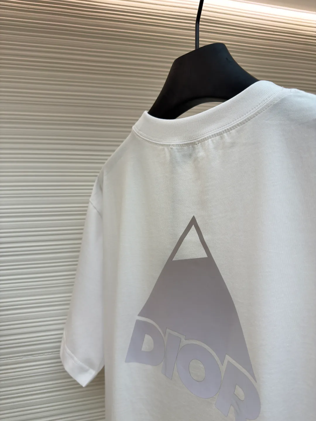 Dior Reflective Triangle Icon Round Neck Short Sleeve ●Item No.: 1681100-A00 ●Fabric: Jersey fabric ●Technology: Reflective lettering and embossed production ●Version: Fitted version ●Weight: about 205 grams ●Size: S-M-L-XL ●Description: The main body is made of 24S special woven compact cotton to make jersey fabric, weight 180g. High-count combed cotton yarn eliminates most of the short hairiness through compact spinning process, making the yarn smoother and stronger. The woven fabric structure is extremely dense, flat and soft, with excellent anti-pilling ability and durability, while retaining the natural advantages of pure cotton, which is breathable and skin-friendly. The neckline is made of 32S 1x1 rib with a weight of 300g. The finer yarn count creates a more delicate and tight thread, which provides better elasticity and deformation resistance than ordinary ribs, ensuring that the neckline can still remain stiff after being put on and taken off many times. The reflective engraving and embossing process is a sophisticated technology that combines safety functions with visual aesthetics. The core is to use a reflective lettering film with a built-in micro-glass bead layer. First, a high-precision laser cutting machine is used to engrave the outline according to the designed fonts and patterns to ensure that the edges are clear and burr-free. The cut reflective film is accurately attached to the surface of the fabric through heat transfer printing equipment under specific temperature and pressure, so that it is firmly combined with the fabric fibers. The case is matte silver-gray under normal conditions, but when illuminated by light, the micro-glass bead layer can achieve efficient retroreflection and instantly present a striking bright effect. The finished product is washable and abrasion resistant, perfectly meeting the dual needs of sportswear for functionality and visual tension. The overall wiring is straight and delicate, the fabric is comfortable and soft, and the color is consistent without color difference. It can be matched with the same style to create a fashionable look and control various occasions. Customized accessories, complete with three standards, same style for men and women!