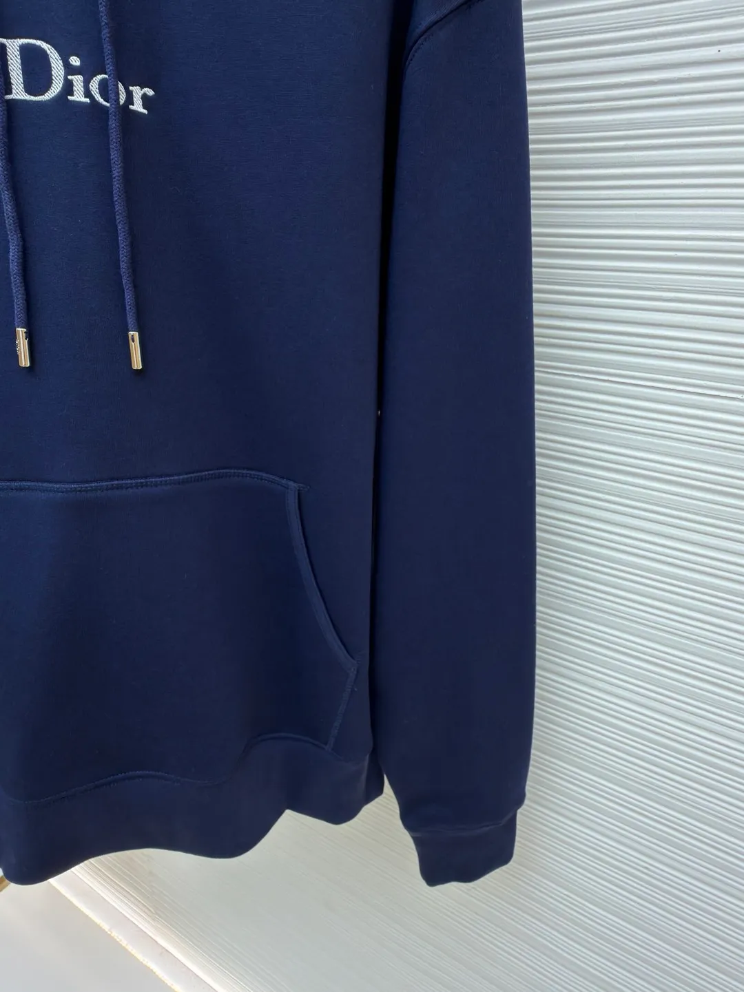 Dior classic logo embroidered hooded sweatshirt ●Item number: 1682333-A75 ●Material: cotton fabric ●Technology: embroidery production ●Color: navy blue ●Version: fitted version ●Weight: about 730 grams ●Size: XS-S-M-L ●Description: It adopts a fleece fabric structure of 26 counts of double yarn + 10S plush bottom, with a weight of 380g/㎡, and 21 counts of 1x1 ribs with a weight of 470g/㎡. It is used for the cuffs and hem. Its extremely high weight ensures the ultimate thickness, stiffness and deformation resistance of these closing parts, forming a unified and strong outline with the body. The fabric is a heavyweight and high-quality sweatshirt fabric. The 26-count double yarn forms a smooth, delicate and strong outer surface of the fabric, ensuring good color fastness and appearance. The 10S plush base undergoes a precise fleece or brushing process to form a layer of rich, dense and uniform fluff on the inside of the fabric. This makes the sweatshirt have a crisp and skeletal feel on the outside and an extremely soft and warm feel on the inside. White tone twill needle embroidery process. Needle embroidery is a straight line embroidery with stitches closely connected and evenly arranged. It is often used to outline clear and sharp outlines. This stitch is used to embroider a diagonal stripe pattern with a certain angle and width. Use white embroidery thread to follow the preset diagonal trajectory and perform precise embroidery with high-density stitches. On the high-weight fabric base, simple, exquisite and three-dimensional line decoration is created. The contrast between white and fabric color is sharp, and the slightly convex texture brought by the embroidery adds a visual and tactile layer, effectively enhancing the exquisite style of the basic sweatshirt. The overall wiring is straight and delicate, the fabric is comfortable and soft, and the color is consistent without color difference. It can be matched with the same style to create a fashionable look and control various occasions. Customized accessories, complete with three standards, same style for men and women!