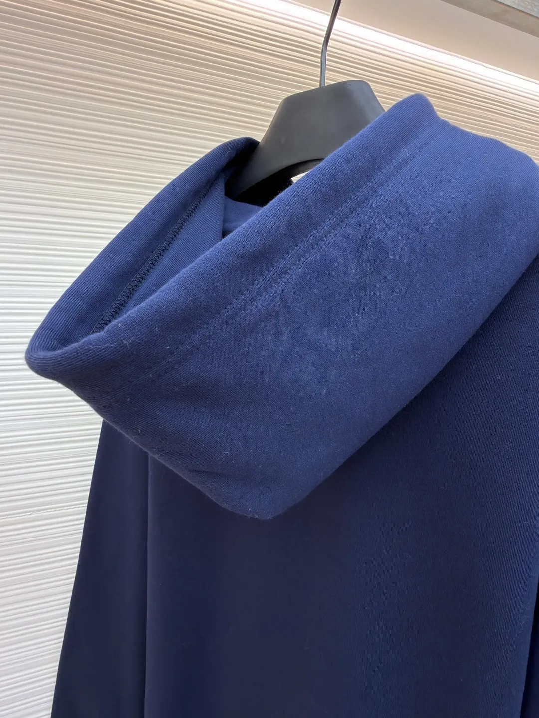 Dior classic logo embroidered hooded sweatshirt ●Item number: 1682333-A75 ●Material: cotton fabric ●Technology: embroidery production ●Color: navy blue ●Version: fitted version ●Weight: about 730 grams ●Size: XS-S-M-L ●Description: It adopts a fleece fabric structure of 26 counts of double yarn + 10S plush bottom, with a weight of 380g/㎡, and 21 counts of 1x1 ribs with a weight of 470g/㎡. It is used for the cuffs and hem. Its extremely high weight ensures the ultimate thickness, stiffness and deformation resistance of these closing parts, forming a unified and strong outline with the body. The fabric is a heavyweight and high-quality sweatshirt fabric. The 26-count double yarn forms a smooth, delicate and strong outer surface of the fabric, ensuring good color fastness and appearance. The 10S plush base undergoes a precise fleece or brushing process to form a layer of rich, dense and uniform fluff on the inside of the fabric. This makes the sweatshirt have a crisp and skeletal feel on the outside and an extremely soft and warm feel on the inside. White tone twill needle embroidery process. Needle embroidery is a straight line embroidery with stitches closely connected and evenly arranged. It is often used to outline clear and sharp outlines. This stitch is used to embroider a diagonal stripe pattern with a certain angle and width. Use white embroidery thread to follow the preset diagonal trajectory and perform precise embroidery with high-density stitches. On the high-weight fabric base, simple, exquisite and three-dimensional line decoration is created. The contrast between white and fabric color is sharp, and the slightly convex texture brought by the embroidery adds a visual and tactile layer, effectively enhancing the exquisite style of the basic sweatshirt. The overall wiring is straight and delicate, the fabric is comfortable and soft, and the color is consistent without color difference. It can be matched with the same style to create a fashionable look and control various occasions. Customized accessories, complete with three standards, same style for men and women!
