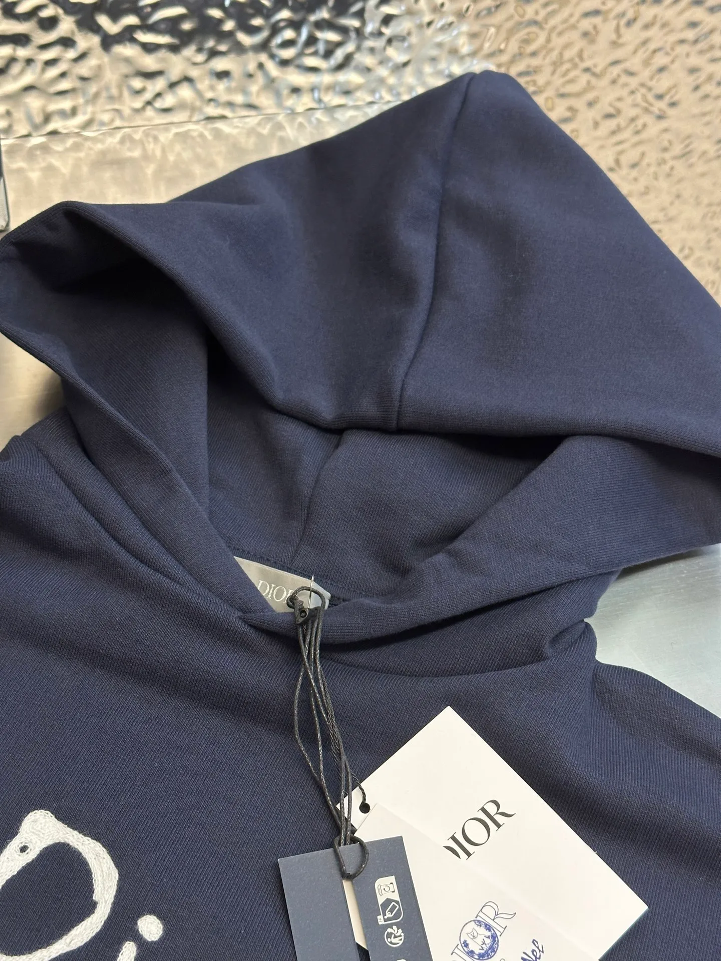 🅿️500 Dior Friends letter embroidered hooded sweatshirt. Cotton fleece fish scale bottom fabric. The surface of the 32-count double-yarn woven fabric is fine and tight, and it feels soft and comfortable. The weight of 50g and the bottom design of 10-count yarn make the fabric have good warmth retention and durability. Thanks to the relatively fine yarns used, this sweatshirt fabric is soft to the touch and comfortable to wear. The design of the fish scale base also increases the skin-friendliness of the fabric, making the wearing experience better. This fabric maintains softness while also possessing good wear-resistance and wrinkle-resistance.  The joint series logo is chain embroidery. Chain embroidery is named because the visual effect of the embroidery is like a chain. The shape is like the links on the chain. It is commonly known as chain embroidery and also called chain eye embroidery. Follow the chain stitch stitch method and embroider from right to left. Maintain the tension of the embroidery thread and the uniformity of the stitches to ensure the three-dimensionality and exquisiteness of the embroidery. It combines the stitching method of chain embroidery with the material of fine wool to create embroidery with chain-like texture and three-dimensional effect.  The hooded drop-shoulder is a loose fit, because it is quite loosely cut, and the shoulder line is large. The drop-shoulder design has no limit on shoulder width. The hem and cuffs are spliced ​​with ribs, which can provide wind protection; the hooded sweatshirt maintains a certain degree of looseness while maintaining a slim fit. The length of the sweatshirt is moderate, which can show the curves of the figure and present an elegant and fashionable feeling.  size：xs s m l