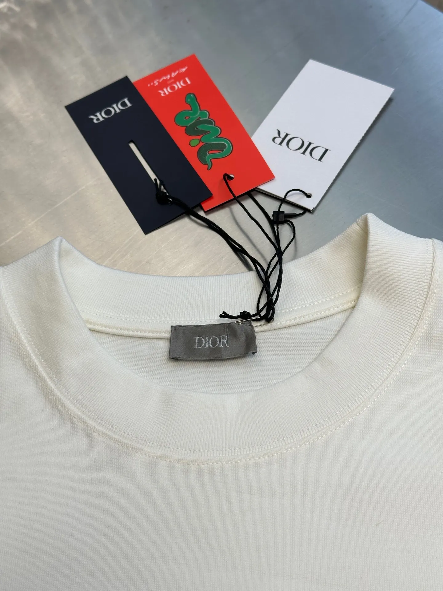 🅿️330 Dior Year of the Snake co-branded bloom-dyed short-sleeves are made of 21s double yarn cotton plain weave. Weighing 320g, it is equipped with 21 pairs of fine cotton yarns and 1*1 horizontal machine woven threads. The front and rear hems are printed with digital direct-injection printing, with large-size patterns throughout.  The front panel is embroidered with a Tajima embroidery machine imported from Japan. The number of embroidery stitches reaches 130,000. The thread color is matched with satin patch to increase stiffness to avoid shifting during the embroidery process. The three-layer embroidery method of short-needle tatami is matched with the new Year of Snake co-branded hangtag size: xs s m l