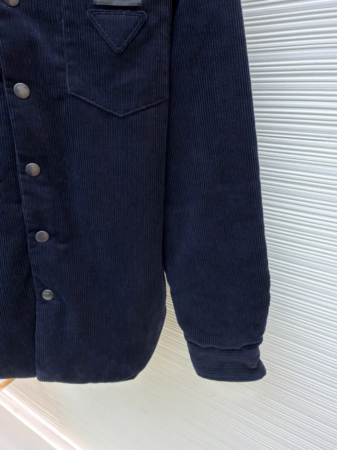 Prada pocket triangle logo corduroy cotton jacket ●Original version: Purchased and developed for 16999 ●Item number: 1681386-B80 ●Fabric: corduroy fabric ●Technology: made on positioning cutting machine ●Color: navy ●Version: fitted version ●Weight: about 820 grams ●Size: S-M-L-XL ●Description: This item is made of high-quality corduroy fabric, and the main tone of dark blue presents a retro texture. It has a lapel design and a metal button placket, which is classic and tool-style. The single patch pocket on the front chest is decorated with the brand's iconic triangle logo, which presents a three-dimensional structure through precision sewing; the corduroy fabric has been specially washed to give it a soft and aged texture, with a soft touch and clear texture. In terms of sewing process, the seams are neatly and firmly routed, and the buttons are made of high-quality metal material, which is durable. From fabric washing to detail decoration, every process pays attention to the presentation of retro style, integrating workwear elements with retro corduroy technology to present a single product that is both practical and stylish. The overall wiring is straight and delicate, the fabric is comfortable and soft, and the color is consistent without color difference. It can be matched with the same style to create a fashionable look and control various occasions. Customized accessories, complete with three standards, same style for men and women!