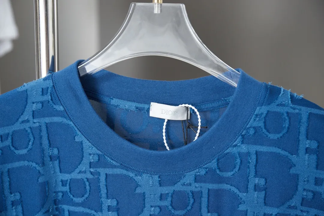 🅿️180 Dior 2025 new style embossed jacquard short-sleeved pure cotton plain fabric, woven with 32S double-strand pure cotton yarn. The 32S double-strand is twisted from two 32-count single yarns. The yarn is thicker and stronger. The fabric has high wear resistance while retaining the moisture absorption and breathability of pure cotton. The plain weave has a tight structure and a smooth surface, but it feels relatively stiff and supports the stiffness of the pattern. The jacquard pattern uses thread-cutting jacquard technology, and the full-width Oblique jacquard pattern forms a relief effect through the deep integration of full-width jacquard and shearing technology. The jacquard structure provides a three-dimensional frame, and the shearing process enhances local texture. The electronic jacquard machine is used to weave complex patterns on the entire fabric to form a three-dimensional concave and convex texture, achieving the integration of texture and pattern. The raised jacquard is cut in a directional manner to create a relief effect, enhancing tactile layering and visual contrast. Straight crew neck fit. Cut and sewn in floral position, standard H hanging fit, with shoulder-length design. The vertical version emphasizes that the width of the shoulders, waist, and hem are basically the same, and it is simple and loose. The short sleeves are tailored to fit the body of the wearer. At the same time, the neckline, cuffs and hem of the short sleeves are all designed with double lines. S M L XL