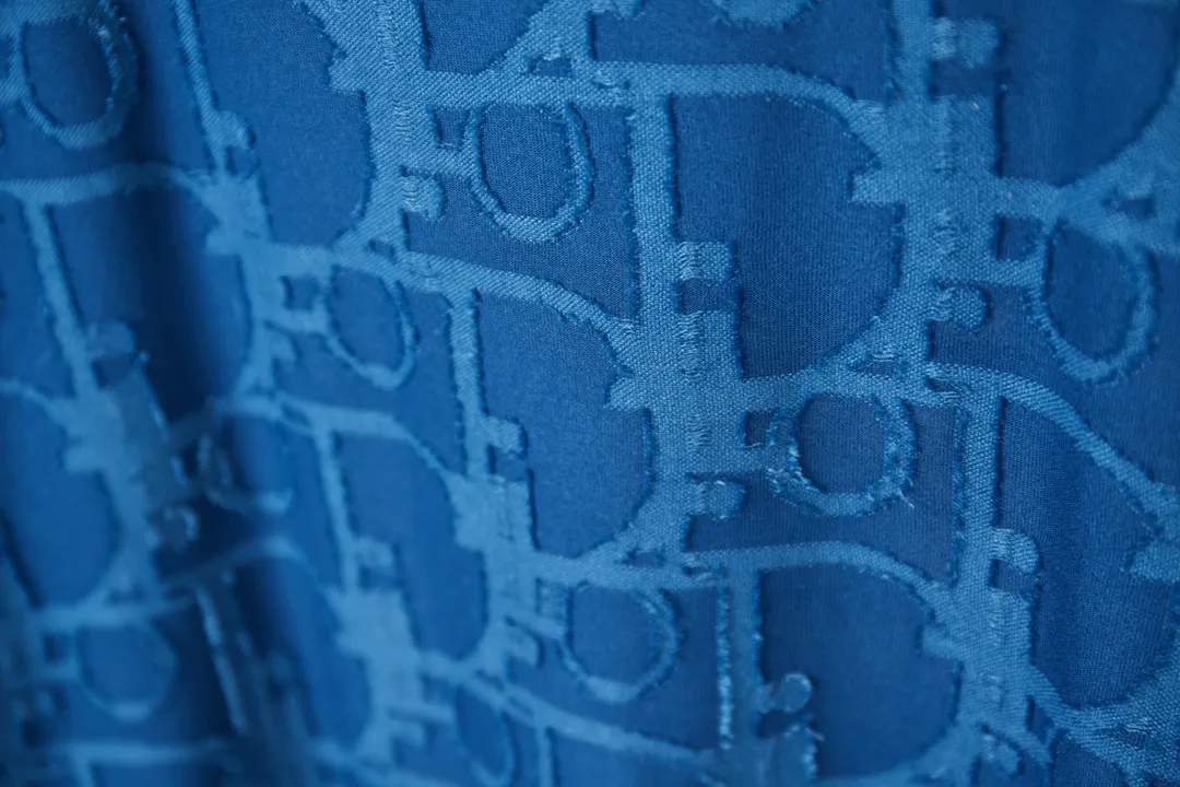 🅿️180 Dior 2025 new style embossed jacquard short-sleeved pure cotton plain fabric, woven with 32S double-strand pure cotton yarn. The 32S double-strand is twisted from two 32-count single yarns. The yarn is thicker and stronger. The fabric has high wear resistance while retaining the moisture absorption and breathability of pure cotton. The plain weave has a tight structure and a smooth surface, but it feels relatively stiff and supports the stiffness of the pattern. The jacquard pattern uses thread-cutting jacquard technology, and the full-width Oblique jacquard pattern forms a relief effect through the deep integration of full-width jacquard and shearing technology. The jacquard structure provides a three-dimensional frame, and the shearing process enhances local texture. The electronic jacquard machine is used to weave complex patterns on the entire fabric to form a three-dimensional concave and convex texture, achieving the integration of texture and pattern. The raised jacquard is cut in a directional manner to create a relief effect, enhancing tactile layering and visual contrast. Straight crew neck fit. Cut and sewn in floral position, standard H hanging fit, with shoulder-length design. The vertical version emphasizes that the width of the shoulders, waist, and hem are basically the same, and it is simple and loose. The short sleeves are tailored to fit the body of the wearer. At the same time, the neckline, cuffs and hem of the short sleeves are all designed with double lines. S M L XL