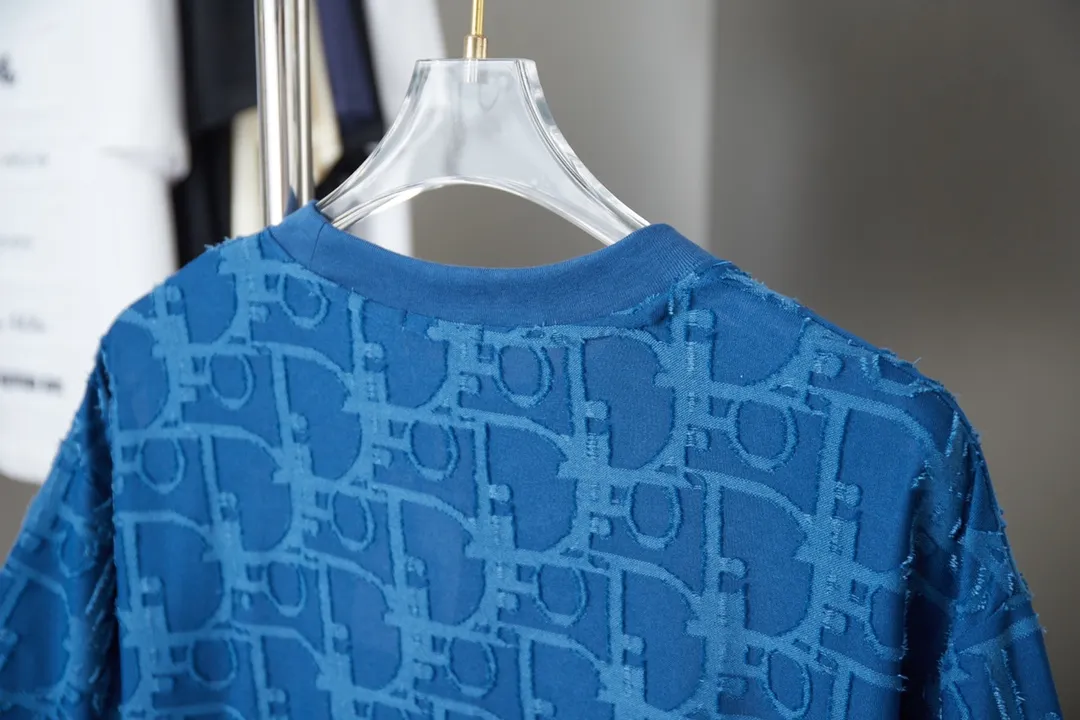 🅿️180 Dior 2025 new style embossed jacquard short-sleeved pure cotton plain fabric, woven with 32S double-strand pure cotton yarn. The 32S double-strand is twisted from two 32-count single yarns. The yarn is thicker and stronger. The fabric has high wear resistance while retaining the moisture absorption and breathability of pure cotton. The plain weave has a tight structure and a smooth surface, but it feels relatively stiff and supports the stiffness of the pattern. The jacquard pattern uses thread-cutting jacquard technology, and the full-width Oblique jacquard pattern forms a relief effect through the deep integration of full-width jacquard and shearing technology. The jacquard structure provides a three-dimensional frame, and the shearing process enhances local texture. The electronic jacquard machine is used to weave complex patterns on the entire fabric to form a three-dimensional concave and convex texture, achieving the integration of texture and pattern. The raised jacquard is cut in a directional manner to create a relief effect, enhancing tactile layering and visual contrast. Straight crew neck fit. Cut and sewn in floral position, standard H hanging fit, with shoulder-length design. The vertical version emphasizes that the width of the shoulders, waist, and hem are basically the same, and it is simple and loose. The short sleeves are tailored to fit the body of the wearer. At the same time, the neckline, cuffs and hem of the short sleeves are all designed with double lines. S M L XL