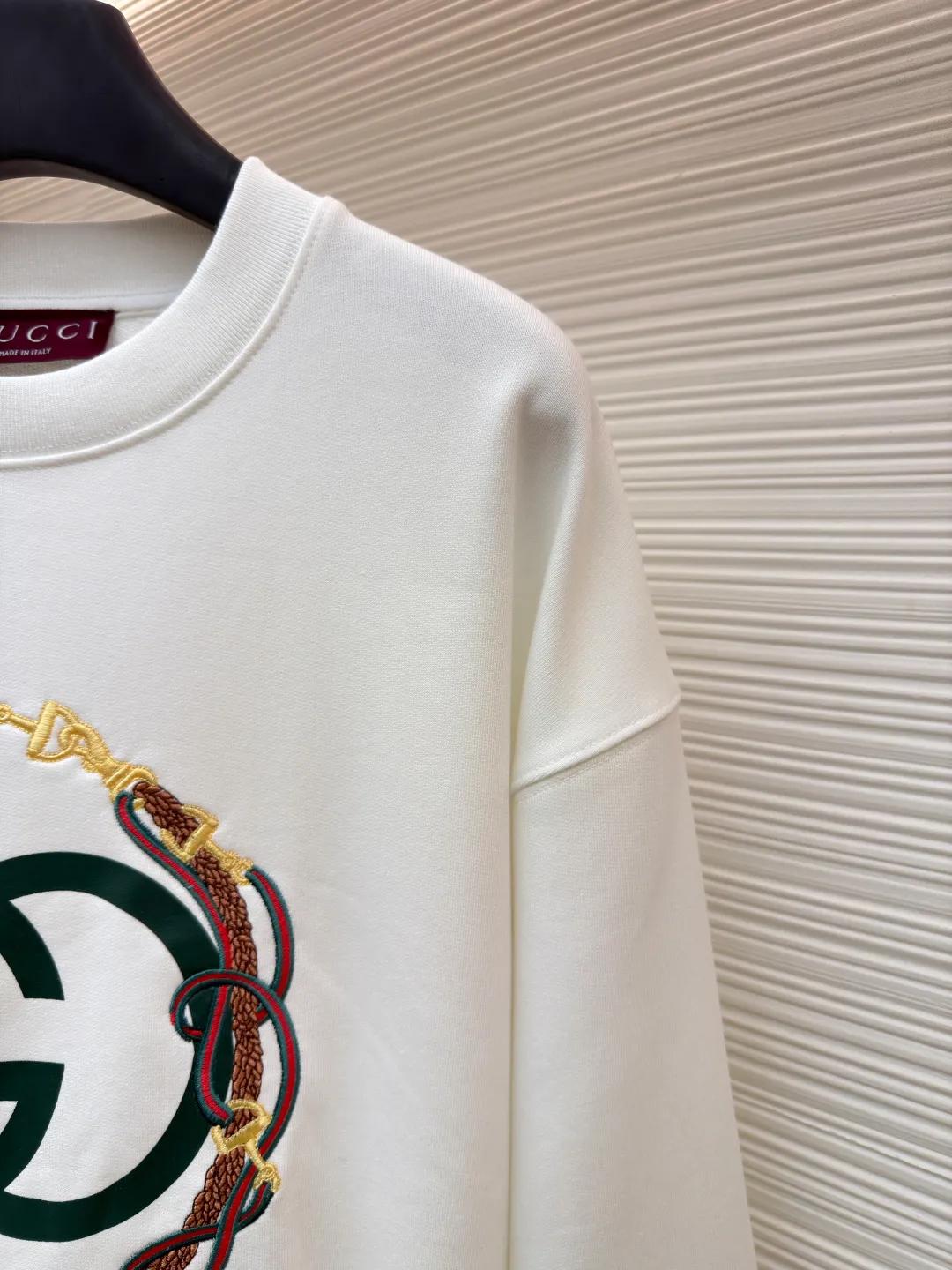 Gucci Bridle Web Round Neck Sweater ●Item No.: 1682279-A65 ●Material: 100% cotton ●Technology: Embroidery ●Color: White ●Version: Fitted ●Weight: about 645 grams ●Size: XS-S-M-L ●Description: This Gucci sweatshirt is made of high-weight combed cotton fabric. The fabric is tight and elastic, which can effectively maintain the stiffness and wearing comfort. The double G logo on the front adopts multi-layer embroidery technology, with gold thread to outline the outline, red and green velvet thread to fill the texture, and metallic chain stripe pattern appliqué. The stitches are fine and even, and each embroidery is precisely positioned to form a three-dimensional contrast with the fabric texture. The body is cut according to the loose shoulder design, and the shoulder line splicing adopts overlock stitching technology to reduce friction when wearing; the cuffs and hem are edged with ribs of the same color, which has long-lasting elasticity and is not easy to loosen. Sizes from XS to L are all standardized plate making, with increasing gradients in dimensions such as garment length and shoulder width. The stitching process uses a combination of flat seams and overlock seams to ensure the firmness of the garments and the exquisiteness of details. The overall craftsmanship combines the brand's iconic design with practical wearing performance. The overall wiring is straight and delicate, the fabric is comfortable and soft, and the color is consistent without color difference. It can be matched with the same style to create a fashionable look and control various occasions. Customized accessories, complete with three standards, same style for men and women!