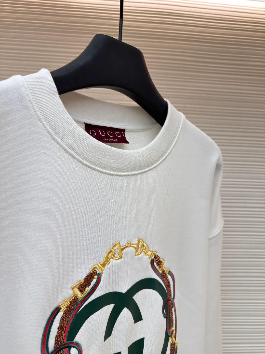 Gucci Bridle Web Round Neck Sweater ●Item No.: 1682279-A65 ●Material: 100% cotton ●Technology: Embroidery ●Color: White ●Version: Fitted ●Weight: about 645 grams ●Size: XS-S-M-L ●Description: This Gucci sweatshirt is made of high-weight combed cotton fabric. The fabric is tight and elastic, which can effectively maintain the stiffness and wearing comfort. The double G logo on the front adopts multi-layer embroidery technology, with gold thread to outline the outline, red and green velvet thread to fill the texture, and metallic chain stripe pattern appliqué. The stitches are fine and even, and each embroidery is precisely positioned to form a three-dimensional contrast with the fabric texture. The body is cut according to the loose shoulder design, and the shoulder line splicing adopts overlock stitching technology to reduce friction when wearing; the cuffs and hem are edged with ribs of the same color, which has long-lasting elasticity and is not easy to loosen. Sizes from XS to L are all standardized plate making, with increasing gradients in dimensions such as garment length and shoulder width. The stitching process uses a combination of flat seams and overlock seams to ensure the firmness of the garments and the exquisiteness of details. The overall craftsmanship combines the brand's iconic design with practical wearing performance. The overall wiring is straight and delicate, the fabric is comfortable and soft, and the color is consistent without color difference. It can be matched with the same style to create a fashionable look and control various occasions. Customized accessories, complete with three standards, same style for men and women!
