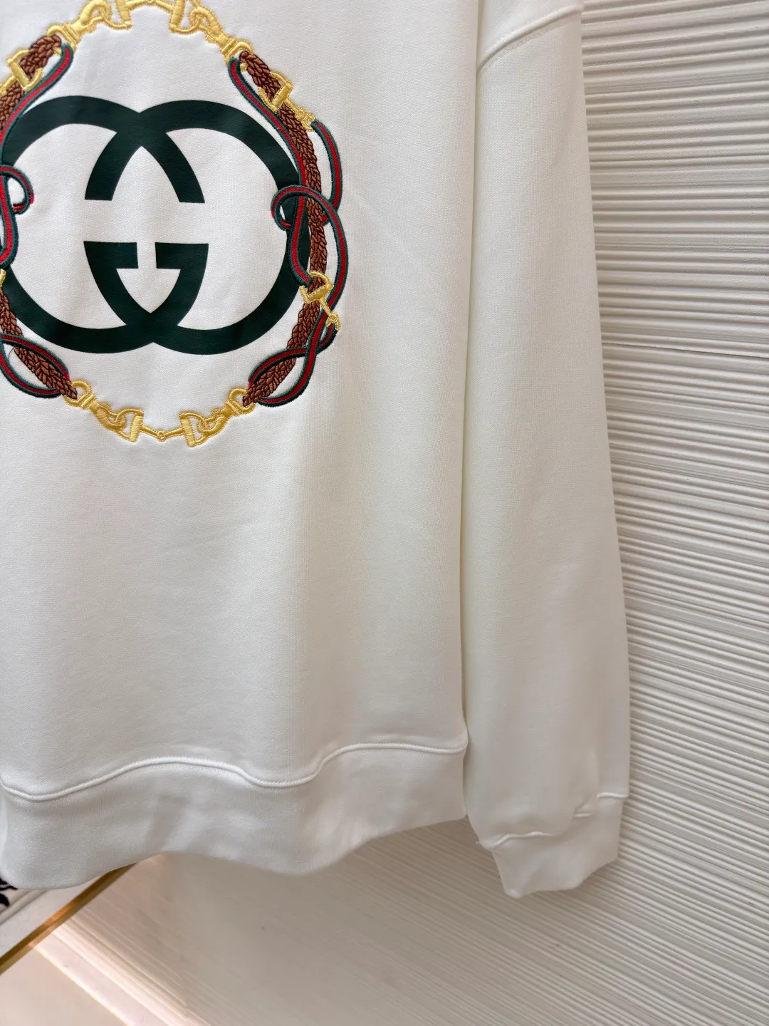 Gucci Bridle Web Round Neck Sweater ●Item No.: 1682279-A65 ●Material: 100% cotton ●Technology: Embroidery ●Color: White ●Version: Fitted ●Weight: about 645 grams ●Size: XS-S-M-L ●Description: This Gucci sweatshirt is made of high-weight combed cotton fabric. The fabric is tight and elastic, which can effectively maintain the stiffness and wearing comfort. The double G logo on the front adopts multi-layer embroidery technology, with gold thread to outline the outline, red and green velvet thread to fill the texture, and metallic chain stripe pattern appliqué. The stitches are fine and even, and each embroidery is precisely positioned to form a three-dimensional contrast with the fabric texture. The body is cut according to the loose shoulder design, and the shoulder line splicing adopts overlock stitching technology to reduce friction when wearing; the cuffs and hem are edged with ribs of the same color, which has long-lasting elasticity and is not easy to loosen. Sizes from XS to L are all standardized plate making, with increasing gradients in dimensions such as garment length and shoulder width. The stitching process uses a combination of flat seams and overlock seams to ensure the firmness of the garments and the exquisiteness of details. The overall craftsmanship combines the brand's iconic design with practical wearing performance. The overall wiring is straight and delicate, the fabric is comfortable and soft, and the color is consistent without color difference. It can be matched with the same style to create a fashionable look and control various occasions. Customized accessories, complete with three standards, same style for men and women!