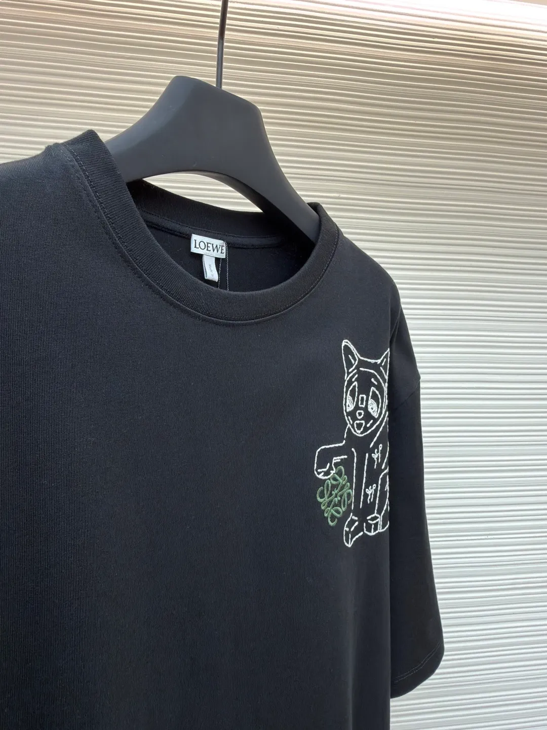 Loewe Cat Line Pattern Round Neck Short Sleeve ●Original version: Purchased and developed at 4330 ●Item number: 1681867-X85 ●Material: combed cotton fabric ●Technology: embroidery production ●Color: black ●Version: fitted version ●Weight: about 295 grams ●Size: XS-S-M-L ●Description: Made of 15S fine cotton plain fabric, 230g; with 32S double yarn thread, 300g. Plain weave fabric made from combed cotton fibers has a more orderly arrangement and higher density than ordinary cotton, so it has better texture and luster. 15S fine cotton plain fabric is a high-quality cotton fabric with the characteristics of softness, comfort, good breathability, and good durability. Anagram Embroidery Lucky Cat: The rice grain line embroidery process uses special ultra-fine embroidery thread and high-density stitching to create a pattern outline as delicate and continuous as grains. Its core feature lies in the precise arrangement of ultra-fine stitches, which require 12-15 stitches per centimeter to form full lines, and the edges present a handmade micro-waving effect. The fabric achieves a stroke-like gradient of thickness and flow. The overall pattern is light, breathable and smooth to the touch. It looks like a line outline from a distance, but the texture of interwoven fibers can be seen up close. It is especially suitable for expressing delicate details such as logo outlines and geometric borders. Anagram embroidery: Using three-dimensional embroidery technology, the logo clearly restores the spacing curve. The mercerized embroidery thread with luster is selected, combined with complex embroidery needlework and fine detail processing to create a three-dimensional relief embroidery effect. Classic trademark letter design, fine embroidery and dense stitching, clear font and strong sense of lines and three-dimensionality. The overall wiring is straight and delicate, the fabric is comfortable and soft, and the color is consistent without color difference. It can be matched with the same style to create a fashionable look and control various occasions. Customized accessories, complete with three standards, same style for men and women!