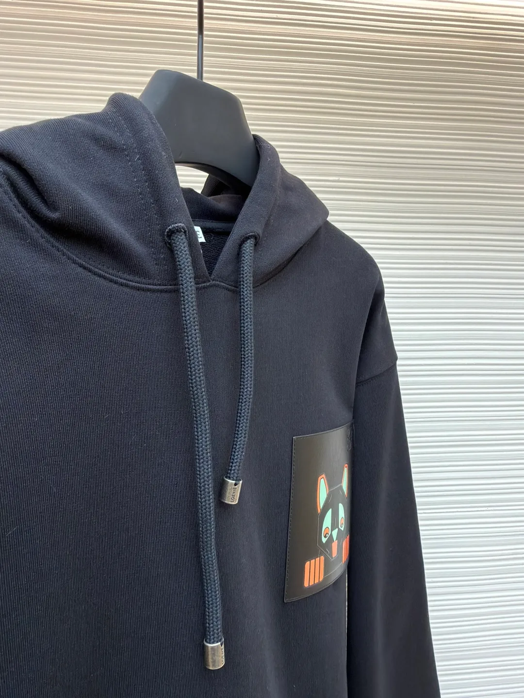 Loewe quirky kitten embossed hooded sweatshirt ●Original version: Purchased and developed by 8718 ●Item number: 1681954-A85 ●Material: pure cotton fabric ●Technology: genuine leather embossed production ●Color: black ●Version: fitted version ●Weight: about 920 grams ●Size: XS-S-M-L ●Description: This LV black hooded sweatshirt is made of 380g heavyweight fleece sweatshirt fabric. It is pre-shrunk and has a stable shape, with a fine matte texture on the surface. The hat rope is made of nylon braided rope + metal bell. The rope head is polished and rhodium-plated, with a cool texture and anti-oxidation. The chest patch pocket uses genuine leather embossing technology: the leather base is embossed with brand dark patterns, and the bag surface pattern uses multi-color silk screen printing + partial flocking. The ears, paws and other details of the animal image are raised by flocking to enhance the three-dimensional effect, and the color fastness reaches level 4 or above. The body stitching adopts double-needle overlocking technology, and the ribbing on the cuffs and hem is made of the same fabric, with an elastic rebound rate of ≥85%. The overall cutting error is controlled within 0.3cm, and the brand logo is embossed on the inside of the neckline, taking into account concealment and recognition, and balancing practicality and design. The overall wiring is straight and delicate, the fabric is comfortable and soft, and the color is consistent without color difference. It can be matched with the same style to create a fashionable look and control various occasions. Customized accessories, complete with three standards, same style for men and women!