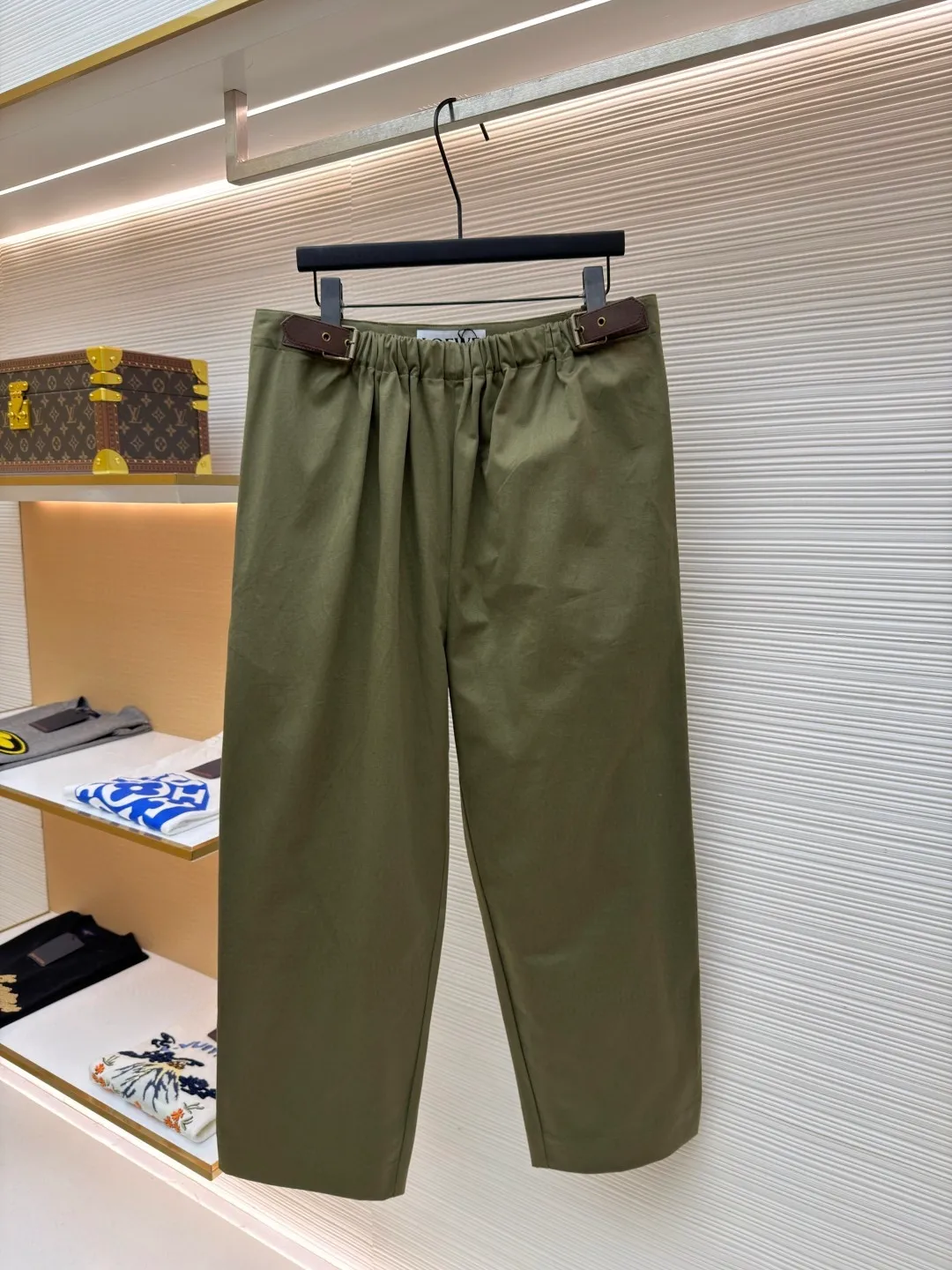 Loewe military green belt trousers ●Original version: purchased and developed by 7161 ●Item number: 1681217-B15 ●Fabric: high weight dyed cotton satin fabric ●Technology: leather patch production ●Color: military green ●Version: loose fit ●Weight: about 530 grams ●Size: 46-48-50-52 ●Description: Made of high-weight cotton satin fabric, high-weight high-temperature dyed cotton satin fabric is a high-end material with excellent texture and functionality. The core of its technology lies in the selection of high-count, long-staple cotton, and the satin weave method to minimize the interweaving points of warp and weft yarns, thereby forming a unique surface that is smooth, supple and with a faint luster. The high weight ensures that the fabric has a tight structure, is crisp and stylish, and has excellent drape and wear resistance. , "Using high-temperature and high-pressure dyeing technology in the dyeing process, the dye molecules can deeply penetrate into the core of the fiber, thereby achieving high color saturation, strong color fastness and not easy to fade. This process not only gives the fabric a rich and lasting color, but also makes it plump and soft to the touch. It also retains the natural breathability of cotton fiber, achieving a both luxurious and practical wearing experience. The contrasting color decorative belt echoes the theme of military uniforms and allows for flexible waist adjustment; the back is embossed with bronzing leather patches, which use high temperature and high pressure. The brand logo is permanently embossed on the leather and sewn onto the back of the jacket. This process makes the pattern clear and durable, becoming a low-key and powerful symbol of the brand's identity. The style adopts a regular fit and a mid-rise straight design to ensure clean lines and comfortable wearing. The front gathers are an important decorative element and provide room for movement in the functional legs. The pocket design is both practical and simple, while the rear button-stuck welt pocket enhances the sophistication of workwear style.