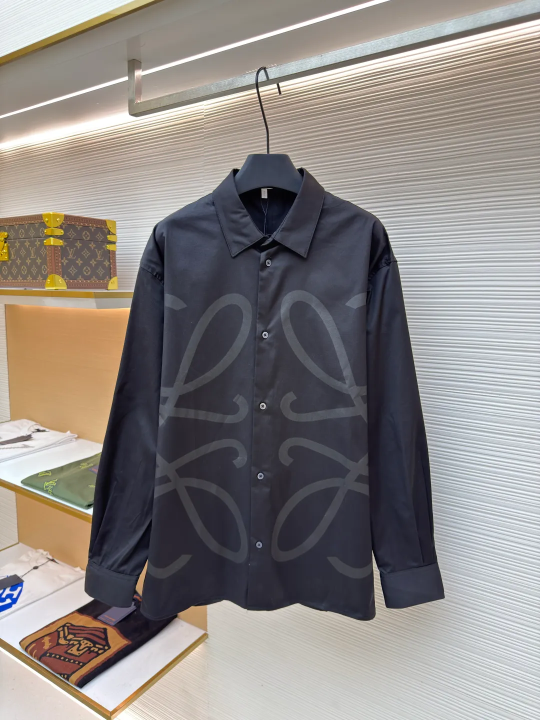 Loewe concealed logo lapel shirt ●Original version: Purchased and developed by 6454 ●Item number: 1680723-A75 ●Fabric: Light cotton poplin shirt fabric ●Technology: Printing ●Version: Fitted version ●Weight: about 290 grams ●Size: 36-38-40-42 ●Description: Poplin is a classic cotton fabric characterized by a large density difference between warp and weft yarns, forming a fine diamond-shaped grainy texture. This structure not only gives the fabric a refreshing and breathable wearing feel, but also ensures that its texture is light and thin but has a crisp texture, avoiding the shortcomings of ordinary thin cotton that easily collapses, perfectly supporting the neat silhouette of the shirt, while maintaining the unique skin-friendly comfort of cotton. The chest is decorated with a discharge printing process; discharge printing is a special process that erodes through the dyed base fabric to reveal the light-colored pattern of the original fabric. This makes the Anagram logo not simply covered on the fabric, but integrated with the fabric, feeling smooth and traceless, showing a low-key and high-end matte effect. Fit and design The shirt adopts a loose fit of standard length; it is precisely tailored to the pattern. It is neither too loose nor deliberately slim, aiming to create a clean silhouette and is extremely tolerant to all body types. The standard length ensures that the hem can be tucked into trousers or hang naturally, meeting a variety of wear needs, including formal and casual. The overall wiring is straight and delicate, the fabric is comfortable and soft, and the color is consistent without color difference. It can be matched with the same style to create a fashionable look and control various occasions. Customized accessories, complete with three standards, same style for men and women!