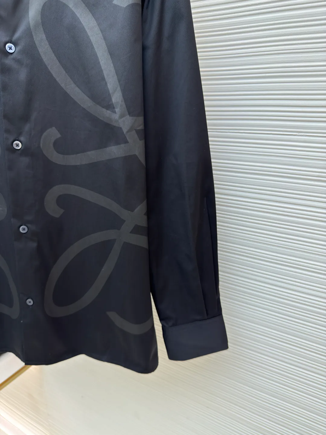 Loewe concealed logo lapel shirt ●Original version: Purchased and developed by 6454 ●Item number: 1680723-A75 ●Fabric: Light cotton poplin shirt fabric ●Technology: Printing ●Version: Fitted version ●Weight: about 290 grams ●Size: 36-38-40-42 ●Description: Poplin is a classic cotton fabric characterized by a large density difference between warp and weft yarns, forming a fine diamond-shaped grainy texture. This structure not only gives the fabric a refreshing and breathable wearing feel, but also ensures that its texture is light and thin but has a crisp texture, avoiding the shortcomings of ordinary thin cotton that easily collapses, perfectly supporting the neat silhouette of the shirt, while maintaining the unique skin-friendly comfort of cotton. The chest is decorated with a discharge printing process; discharge printing is a special process that erodes through the dyed base fabric to reveal the light-colored pattern of the original fabric. This makes the Anagram logo not simply covered on the fabric, but integrated with the fabric, feeling smooth and traceless, showing a low-key and high-end matte effect. Fit and design The shirt adopts a loose fit of standard length; it is precisely tailored to the pattern. It is neither too loose nor deliberately slim, aiming to create a clean silhouette and is extremely tolerant to all body types. The standard length ensures that the hem can be tucked into trousers or hang naturally, meeting a variety of wear needs, including formal and casual. The overall wiring is straight and delicate, the fabric is comfortable and soft, and the color is consistent without color difference. It can be matched with the same style to create a fashionable look and control various occasions. Customized accessories, complete with three standards, same style for men and women!