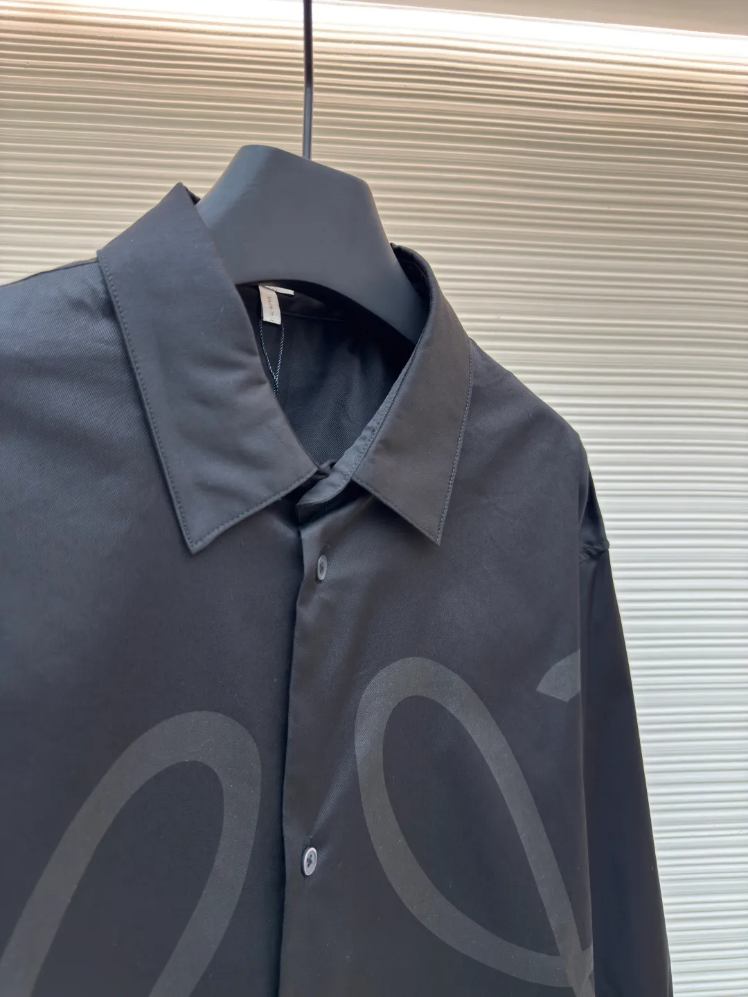 Loewe concealed logo lapel shirt ●Original version: Purchased and developed by 6454 ●Item number: 1680723-A75 ●Fabric: Light cotton poplin shirt fabric ●Technology: Printing ●Version: Fitted version ●Weight: about 290 grams ●Size: 36-38-40-42 ●Description: Poplin is a classic cotton fabric characterized by a large density difference between warp and weft yarns, forming a fine diamond-shaped grainy texture. This structure not only gives the fabric a refreshing and breathable wearing feel, but also ensures that its texture is light and thin but has a crisp texture, avoiding the shortcomings of ordinary thin cotton that easily collapses, perfectly supporting the neat silhouette of the shirt, while maintaining the unique skin-friendly comfort of cotton. The chest is decorated with a discharge printing process; discharge printing is a special process that erodes through the dyed base fabric to reveal the light-colored pattern of the original fabric. This makes the Anagram logo not simply covered on the fabric, but integrated with the fabric, feeling smooth and traceless, showing a low-key and high-end matte effect. Fit and design The shirt adopts a loose fit of standard length; it is precisely tailored to the pattern. It is neither too loose nor deliberately slim, aiming to create a clean silhouette and is extremely tolerant to all body types. The standard length ensures that the hem can be tucked into trousers or hang naturally, meeting a variety of wear needs, including formal and casual. The overall wiring is straight and delicate, the fabric is comfortable and soft, and the color is consistent without color difference. It can be matched with the same style to create a fashionable look and control various occasions. Customized accessories, complete with three standards, same style for men and women!