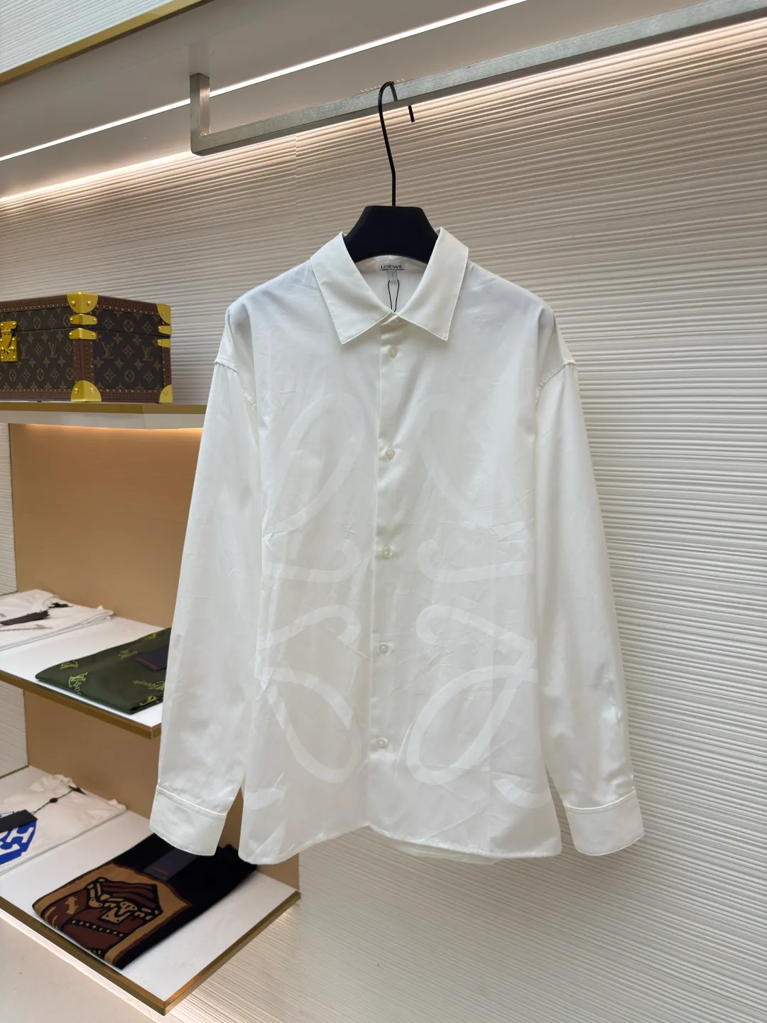 Loewe concealed logo lapel shirt ●Original version: Purchased and developed by 5268 ●Item No.: 1680722-A75 ●Fabric: Light cotton poplin shirt fabric ●Technology: Printing ●Version: Fitted version ●Weight: about 270 grams ●Size: 36-38-40-42 ●Description: Poplin is a classic cotton fabric characterized by a large density difference between warp and weft yarns, forming a fine diamond-shaped grainy texture. This structure not only gives the fabric a refreshing and breathable wearing feel, but also ensures that its texture is light and thin but has a crisp texture, avoiding the shortcomings of ordinary thin cotton that easily collapses, perfectly supporting the neat silhouette of the shirt, while maintaining the unique skin-friendly comfort of cotton. The chest is decorated with a discharge printing process; discharge printing is a special process that erodes through the dyed base fabric to reveal the light-colored pattern of the original fabric. This makes the Anagram logo not simply covered on the fabric, but integrated with the fabric, feeling smooth and traceless, showing a low-key and high-end matte effect. Fit and design The shirt adopts a loose fit of standard length; it is precisely tailored to the pattern. It is neither too loose nor deliberately slim, aiming to create a clean silhouette and is extremely tolerant to all body types. The standard length ensures that the hem can be tucked into trousers or hang naturally, meeting a variety of wear needs, including formal and casual. The overall wiring is straight and delicate, the fabric is comfortable and soft, and the color is consistent without color difference. It can be matched with the same style to create a fashionable look and control various occasions. Customized accessories, complete with three standards, same style for men and women!