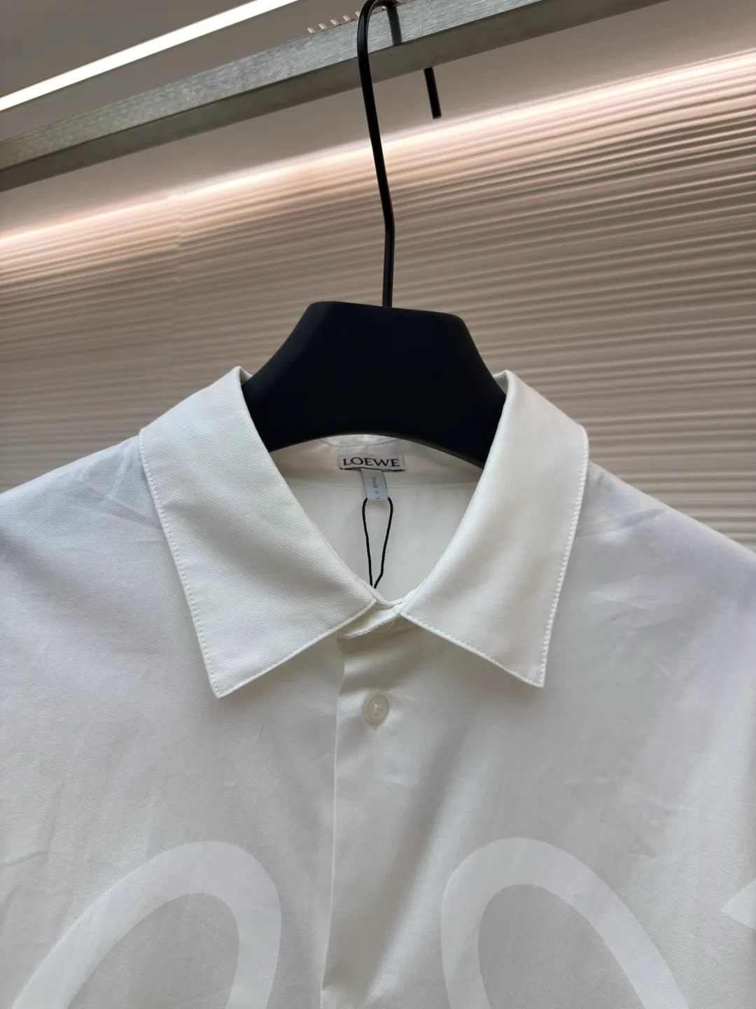 Loewe concealed logo lapel shirt ●Original version: Purchased and developed by 5268 ●Item No.: 1680722-A75 ●Fabric: Light cotton poplin shirt fabric ●Technology: Printing ●Version: Fitted version ●Weight: about 270 grams ●Size: 36-38-40-42 ●Description: Poplin is a classic cotton fabric characterized by a large density difference between warp and weft yarns, forming a fine diamond-shaped grainy texture. This structure not only gives the fabric a refreshing and breathable wearing feel, but also ensures that its texture is light and thin but has a crisp texture, avoiding the shortcomings of ordinary thin cotton that easily collapses, perfectly supporting the neat silhouette of the shirt, while maintaining the unique skin-friendly comfort of cotton. The chest is decorated with a discharge printing process; discharge printing is a special process that erodes through the dyed base fabric to reveal the light-colored pattern of the original fabric. This makes the Anagram logo not simply covered on the fabric, but integrated with the fabric, feeling smooth and traceless, showing a low-key and high-end matte effect. Fit and design The shirt adopts a loose fit of standard length; it is precisely tailored to the pattern. It is neither too loose nor deliberately slim, aiming to create a clean silhouette and is extremely tolerant to all body types. The standard length ensures that the hem can be tucked into trousers or hang naturally, meeting a variety of wear needs, including formal and casual. The overall wiring is straight and delicate, the fabric is comfortable and soft, and the color is consistent without color difference. It can be matched with the same style to create a fashionable look and control various occasions. Customized accessories, complete with three standards, same style for men and women!
