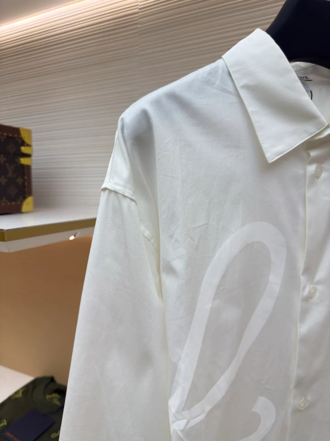 Loewe concealed logo lapel shirt ●Original version: Purchased and developed by 5268 ●Item No.: 1680722-A75 ●Fabric: Light cotton poplin shirt fabric ●Technology: Printing ●Version: Fitted version ●Weight: about 270 grams ●Size: 36-38-40-42 ●Description: Poplin is a classic cotton fabric characterized by a large density difference between warp and weft yarns, forming a fine diamond-shaped grainy texture. This structure not only gives the fabric a refreshing and breathable wearing feel, but also ensures that its texture is light and thin but has a crisp texture, avoiding the shortcomings of ordinary thin cotton that easily collapses, perfectly supporting the neat silhouette of the shirt, while maintaining the unique skin-friendly comfort of cotton. The chest is decorated with a discharge printing process; discharge printing is a special process that erodes through the dyed base fabric to reveal the light-colored pattern of the original fabric. This makes the Anagram logo not simply covered on the fabric, but integrated with the fabric, feeling smooth and traceless, showing a low-key and high-end matte effect. Fit and design The shirt adopts a loose fit of standard length; it is precisely tailored to the pattern. It is neither too loose nor deliberately slim, aiming to create a clean silhouette and is extremely tolerant to all body types. The standard length ensures that the hem can be tucked into trousers or hang naturally, meeting a variety of wear needs, including formal and casual. The overall wiring is straight and delicate, the fabric is comfortable and soft, and the color is consistent without color difference. It can be matched with the same style to create a fashionable look and control various occasions. Customized accessories, complete with three standards, same style for men and women!
