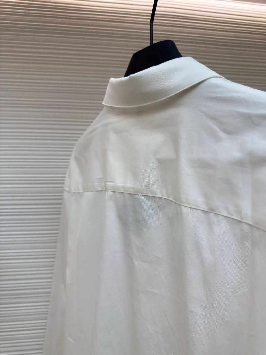 Loewe concealed logo lapel shirt ●Original version: Purchased and developed by 5268 ●Item No.: 1680722-A75 ●Fabric: Light cotton poplin shirt fabric ●Technology: Printing ●Version: Fitted version ●Weight: about 270 grams ●Size: 36-38-40-42 ●Description: Poplin is a classic cotton fabric characterized by a large density difference between warp and weft yarns, forming a fine diamond-shaped grainy texture. This structure not only gives the fabric a refreshing and breathable wearing feel, but also ensures that its texture is light and thin but has a crisp texture, avoiding the shortcomings of ordinary thin cotton that easily collapses, perfectly supporting the neat silhouette of the shirt, while maintaining the unique skin-friendly comfort of cotton. The chest is decorated with a discharge printing process; discharge printing is a special process that erodes through the dyed base fabric to reveal the light-colored pattern of the original fabric. This makes the Anagram logo not simply covered on the fabric, but integrated with the fabric, feeling smooth and traceless, showing a low-key and high-end matte effect. Fit and design The shirt adopts a loose fit of standard length; it is precisely tailored to the pattern. It is neither too loose nor deliberately slim, aiming to create a clean silhouette and is extremely tolerant to all body types. The standard length ensures that the hem can be tucked into trousers or hang naturally, meeting a variety of wear needs, including formal and casual. The overall wiring is straight and delicate, the fabric is comfortable and soft, and the color is consistent without color difference. It can be matched with the same style to create a fashionable look and control various occasions. Customized accessories, complete with three standards, same style for men and women!
