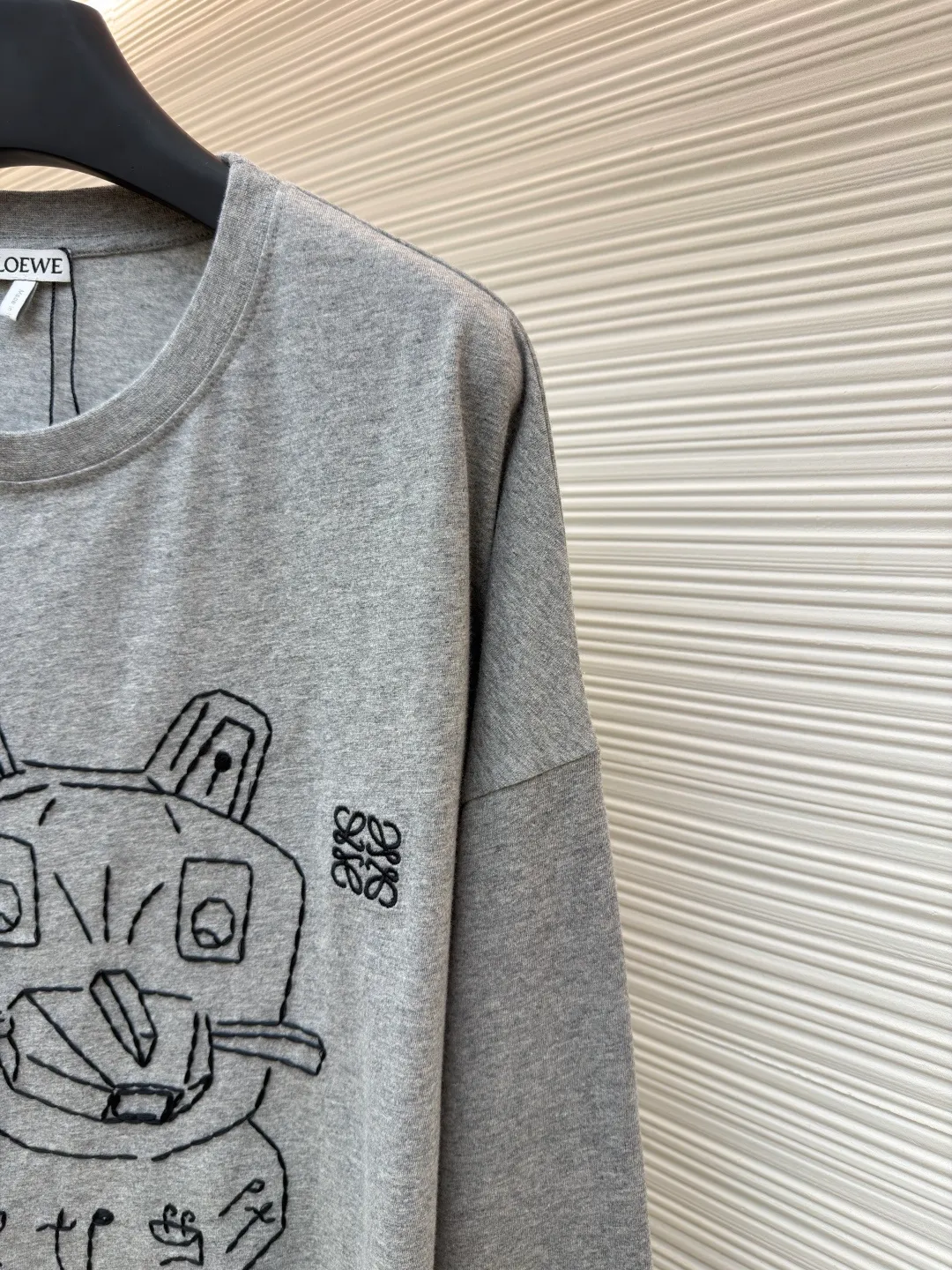 Loewe Stone Cat Round Neck Long Sleeve ●Original version: Purchased and developed by 5148 ●Item number: 1681939-A15 ●Fabric: Cotton jersey fabric ●Technology: Rice grain line embroidery production ●Color: gray ●Version: Fitted version ●Weight: about 250 grams ●Size: High-count combed cotton yarn eliminates most of the short hairiness through compact spinning process, making the yarn smoother and stronger. The woven fabric structure is extremely dense, flat and soft, with excellent anti-pilling ability and durability, while retaining the natural advantages of pure cotton, which is breathable and skin-friendly. The neckline is made of 32S 1x1 rib with a weight of 300g. The finer yarn count creates a more delicate and tight thread, which provides better resilience and anti-deformation than ordinary ribs, ensuring that the neckline can still remain stiff after being put on and taken off many times. The rice grain line embroidery process uses special ultra-fine embroidery thread and high-density stitching to create a pattern outline as delicate and continuous as grains. Its core feature lies in the precise arrangement of ultra-fine stitches, which require 12-15 stitches per centimeter to form full lines, and the edges present a handmade micro-waving effect. The fabric achieves a stroke-like gradient of thickness and flow. The overall pattern is light, breathable and smooth to the touch. It looks like a line outline from a distance, but the texture of interwoven fibers can be seen up close. It is especially suitable for expressing delicate details such as logo outlines and geometric borders. Anagram embroidery: Using three-dimensional embroidery technology, the logo clearly restores the spacing curve. The mercerized embroidery thread with luster is selected, combined with complex embroidery needlework and fine detail processing to create a three-dimensional relief embroidery effect. Classic trademark letter design, fine embroidery and dense stitching, clear font and strong sense of lines and three-dimensionality. The overall wiring is straight and delicate, the fabric is comfortable and soft, and the color is consistent without color difference. It can be matched with the same style to create a fashionable look and control various occasions. Customized accessories, complete with three standards, same style for men and women!