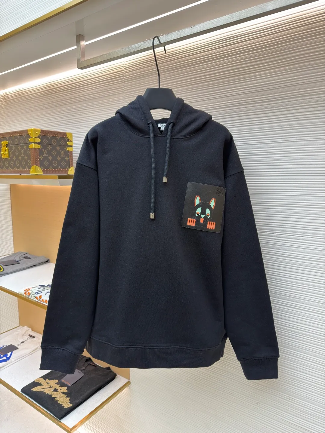 Loewe quirky kitten embossed hooded sweatshirt ●Original version: Purchased and developed by 8718 ●Item number: 1681954-A85 ●Material: pure cotton fabric ●Technology: genuine leather embossed production ●Color: black ●Version: fitted version ●Weight: about 920 grams ●Size: XS-S-M-L ●Description: This LV black hooded sweatshirt is made of 380g heavyweight fleece sweatshirt fabric. It is pre-shrunk and has a stable shape, with a fine matte texture on the surface. The hat rope is made of nylon braided rope + metal bell. The rope head is polished and rhodium-plated, with a cool texture and anti-oxidation. The chest patch pocket uses genuine leather embossing technology: the leather base is embossed with brand dark patterns, and the bag surface pattern uses multi-color silk screen printing + partial flocking. The ears, paws and other details of the animal image are raised by flocking to enhance the three-dimensional effect, and the color fastness reaches level 4 or above. The body stitching adopts double-needle overlocking technology, and the ribbing on the cuffs and hem is made of the same fabric, with an elastic rebound rate of ≥85%. The overall cutting error is controlled within 0.3cm, and the brand logo is embossed on the inside of the neckline, taking into account concealment and recognition, and balancing practicality and design. The overall wiring is straight and delicate, the fabric is comfortable and soft, and the color is consistent without color difference. It can be matched with the same style to create a fashionable look and control various occasions. Customized accessories, complete with three standards, same style for men and women!