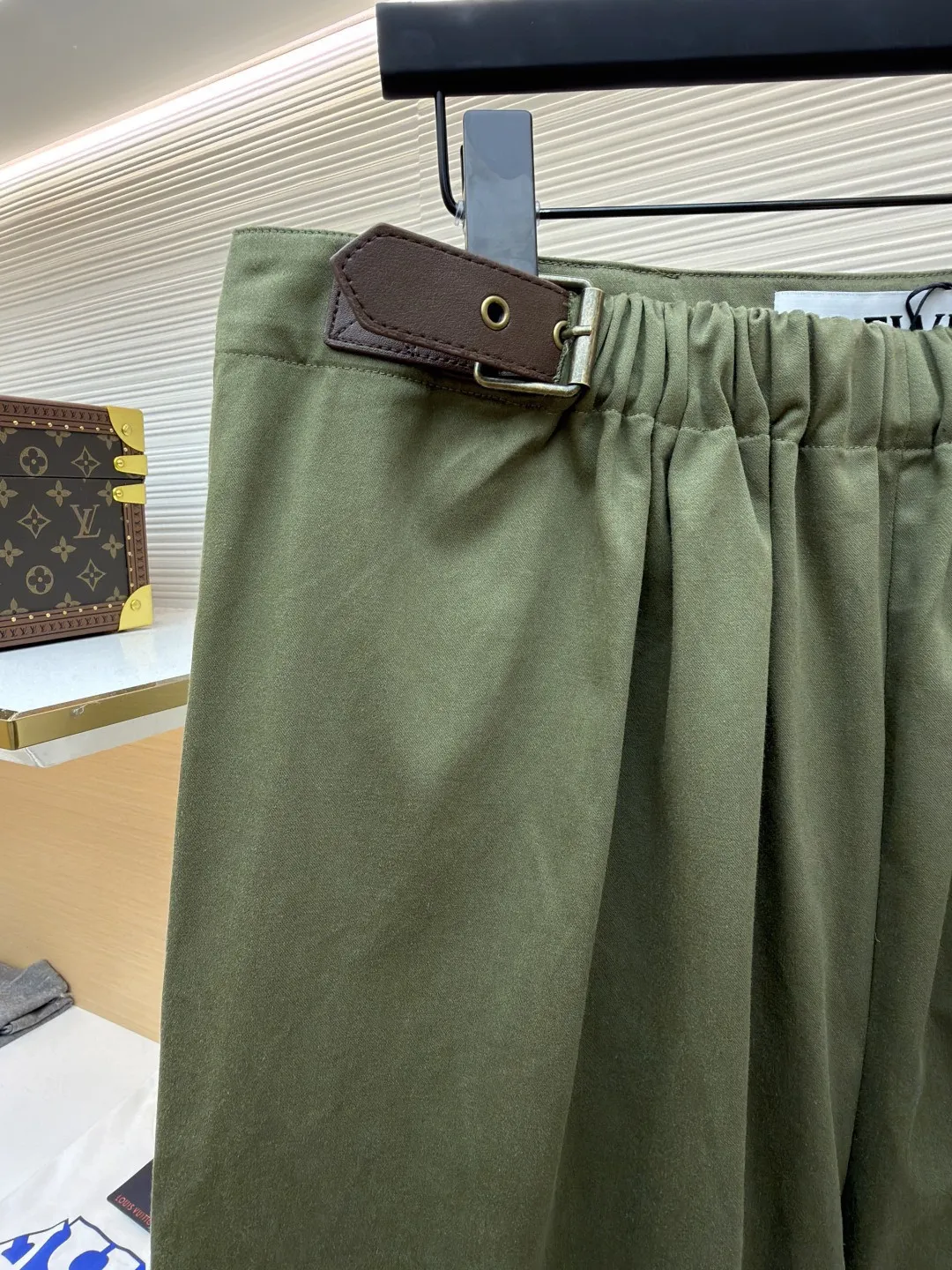 Loewe military green belt trousers ●Original version: purchased and developed by 7161 ●Item number: 1681217-B15 ●Fabric: high weight dyed cotton satin fabric ●Technology: leather patch production ●Color: military green ●Version: loose fit ●Weight: about 530 grams ●Size: 46-48-50-52 ●Description: Made of high-weight cotton satin fabric, high-weight high-temperature dyed cotton satin fabric is a high-end material with excellent texture and functionality. The core of its technology lies in the selection of high-count, long-staple cotton, and the satin weave method to minimize the interweaving points of warp and weft yarns, thereby forming a unique surface that is smooth, supple and with a faint luster. The high weight ensures that the fabric has a tight structure, is crisp and stylish, and has excellent drape and wear resistance. , "Using high-temperature and high-pressure dyeing technology in the dyeing process, the dye molecules can deeply penetrate into the core of the fiber, thereby achieving high color saturation, strong color fastness and not easy to fade. This process not only gives the fabric a rich and lasting color, but also makes it plump and soft to the touch. It also retains the natural breathability of cotton fiber, achieving a both luxurious and practical wearing experience. The contrasting color decorative belt echoes the theme of military uniforms and allows for flexible waist adjustment; the back is embossed with bronzing leather patches, which use high temperature and high pressure. The brand logo is permanently embossed on the leather and sewn onto the back of the jacket. This process makes the pattern clear and durable, becoming a low-key and powerful symbol of the brand's identity. The style adopts a regular fit and a mid-rise straight design to ensure clean lines and comfortable wearing. The front gathers are an important decorative element and provide room for movement in the functional legs. The pocket design is both practical and simple, while the rear button-stuck welt pocket enhances the sophistication of workwear style.