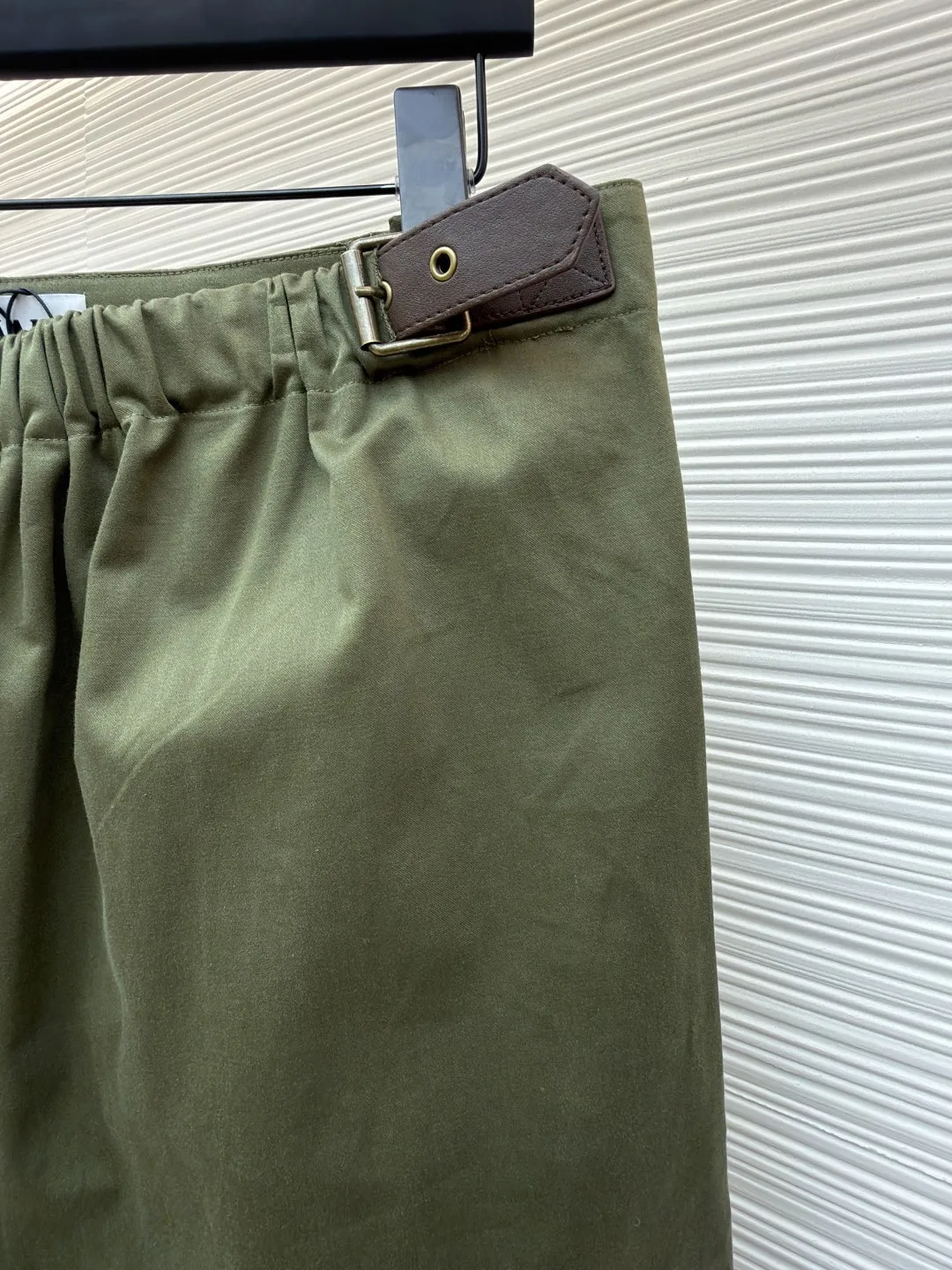 Loewe military green belt trousers ●Original version: purchased and developed by 7161 ●Item number: 1681217-B15 ●Fabric: high weight dyed cotton satin fabric ●Technology: leather patch production ●Color: military green ●Version: loose fit ●Weight: about 530 grams ●Size: 46-48-50-52 ●Description: Made of high-weight cotton satin fabric, high-weight high-temperature dyed cotton satin fabric is a high-end material with excellent texture and functionality. The core of its technology lies in the selection of high-count, long-staple cotton, and the satin weave method to minimize the interweaving points of warp and weft yarns, thereby forming a unique surface that is smooth, supple and with a faint luster. The high weight ensures that the fabric has a tight structure, is crisp and stylish, and has excellent drape and wear resistance. , "Using high-temperature and high-pressure dyeing technology in the dyeing process, the dye molecules can deeply penetrate into the core of the fiber, thereby achieving high color saturation, strong color fastness and not easy to fade. This process not only gives the fabric a rich and lasting color, but also makes it plump and soft to the touch. It also retains the natural breathability of cotton fiber, achieving a both luxurious and practical wearing experience. The contrasting color decorative belt echoes the theme of military uniforms and allows for flexible waist adjustment; the back is embossed with bronzing leather patches, which use high temperature and high pressure. The brand logo is permanently embossed on the leather and sewn onto the back of the jacket. This process makes the pattern clear and durable, becoming a low-key and powerful symbol of the brand's identity. The style adopts a regular fit and a mid-rise straight design to ensure clean lines and comfortable wearing. The front gathers are an important decorative element and provide room for movement in the functional legs. The pocket design is both practical and simple, while the rear button-stuck welt pocket enhances the sophistication of workwear style.