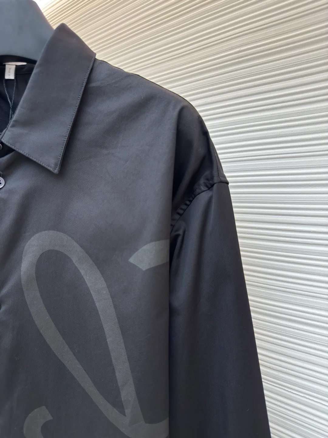 Loewe concealed logo lapel shirt ●Original version: Purchased and developed by 6454 ●Item number: 1680723-A75 ●Fabric: Light cotton poplin shirt fabric ●Technology: Printing ●Version: Fitted version ●Weight: about 290 grams ●Size: 36-38-40-42 ●Description: Poplin is a classic cotton fabric characterized by a large density difference between warp and weft yarns, forming a fine diamond-shaped grainy texture. This structure not only gives the fabric a refreshing and breathable wearing feel, but also ensures that its texture is light and thin but has a crisp texture, avoiding the shortcomings of ordinary thin cotton that easily collapses, perfectly supporting the neat silhouette of the shirt, while maintaining the unique skin-friendly comfort of cotton. The chest is decorated with a discharge printing process; discharge printing is a special process that erodes through the dyed base fabric to reveal the light-colored pattern of the original fabric. This makes the Anagram logo not simply covered on the fabric, but integrated with the fabric, feeling smooth and traceless, showing a low-key and high-end matte effect. Fit and design The shirt adopts a loose fit of standard length; it is precisely tailored to the pattern. It is neither too loose nor deliberately slim, aiming to create a clean silhouette and is extremely tolerant to all body types. The standard length ensures that the hem can be tucked into trousers or hang naturally, meeting a variety of wear needs, including formal and casual. The overall wiring is straight and delicate, the fabric is comfortable and soft, and the color is consistent without color difference. It can be matched with the same style to create a fashionable look and control various occasions. Customized accessories, complete with three standards, same style for men and women!