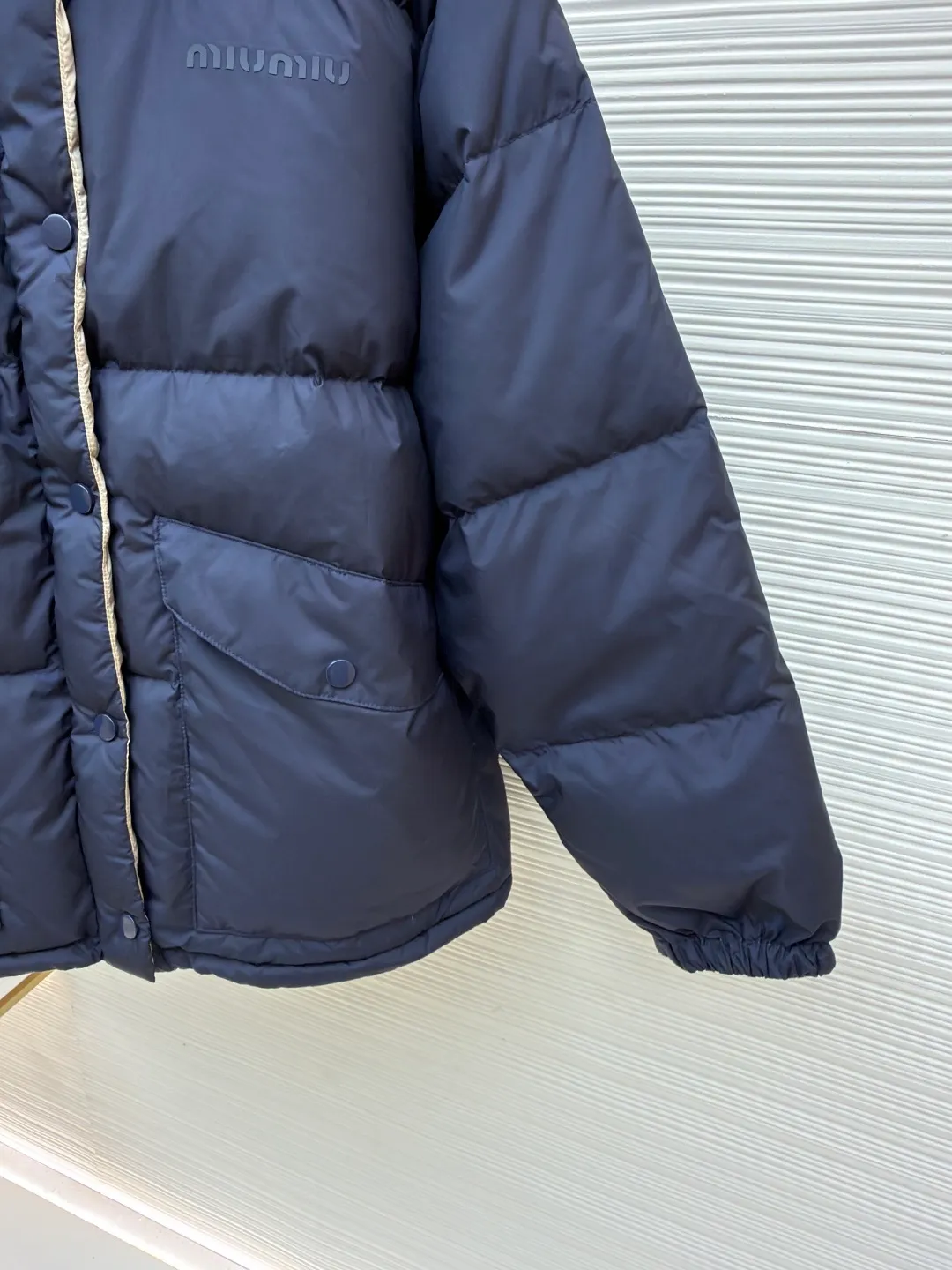 MIUMIU reversible stand collar down jacket ●Original version: purchased and developed by 21060 ●Item number: 1681385-D05 ●Fabric: white duck down fabric ●Technology: mechanical down filling ●Color: navy/khaki ●Version: fitted version ●Weight: about 675 grams ●Size: 36-38-40-42 ●Description: The filling is white duck down with 90% down content, which is one of the gold standards of down quality. "90% down content" means that the down content is extremely high and there are very few impurities such as feather stalks. The down tufts can capture more air and form an efficient thermal insulation layer, thus providing several times the loft and warmth of ordinary down while being lighter in weight. In the double-sided structure, ensuring that the down is evenly distributed between the two layers of fabric without clumping is the core challenge of the down filling process. The stand-up collar design not only improves the neatness of the shape, but also enhances the windproof and warm performance of the neck. Its internal structure needs to be stiff enough to maintain a three-dimensional shape, while at the same time ensuring the comfort of contact with the skin. The precision stitching in conjunction with the overall design not only plays a role in fixing the down and preventing displacement, but the uniformity, tension and pattern of the stitches have become important decorative elements, reflecting rigorous industrial aesthetics. The overall wiring is straight and delicate, the fabric is comfortable and soft, and the color is consistent without color difference. It can be matched with the same style to create a fashionable look and control various occasions. Customized accessories, complete with three standards, same style for men and women!