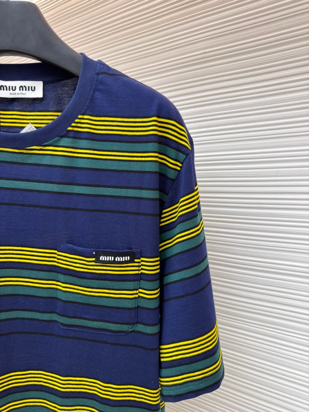 MIUMIU yellow, green and blue striped round neck short sleeves ●Original version: purchased and developed by 4755 ●Item number: 1681739-A10 ●Fabric: Jacquard striped knitted fabric ●Technology: Wool jacquard production ●Color: yellow, green and blue ●Version: Fitted version ●Weight: about 185 grams ●Size: XS-S-M-L ●Description: Using 32S jacquard stripe technology special textile compact cotton , 145g; with 32S double yarn frame, 380g. The fabric is made of 32-count combed cotton yarn and has been processed by compact spinning technology, so that the yarn fibers are tightly arranged and impurities and hairiness are significantly reduced. The fabric structure is denser and smoother. It not only feels delicate and smooth, but its wear resistance and anti-pilling performance is also far superior to ordinary cotton fabrics. The weight of the fabric ensures that the fabric has good durability while maintaining the natural breathability and skin-friendly properties of cotton. It is very suitable for spring, summer and transitional seasons, and achieves the unity of comfort and quality. The striped effect is achieved through plain knitting technology where colored yarns are alternately woven. This is different from later printing. The color is firm and long-lasting, and the striped edges are clear and neat. The design that combines simple stripes with the possible jacquard texture of the underlying fabric increases the visual layering, avoids monotony, and embodies the design idea of ​​finding sophistication in simplicity. The wool jacquard logo process is a high-end technology that weaves the brand logo directly into the fabric. The warp and weft yarns of the loom are controlled by computer programming, and yarns of different colors are interwoven to form precise and clear patterns on the surface of the sweater. The jacquard process makes the logo and logo fabric seamlessly integrated, with a smooth touch and no bulges, and clear and seamless edges, which greatly improves wearing comfort and aesthetics. The overall wiring is straight and delicate, the fabric is comfortable and soft, and the color is consistent without color difference. It can be matched with the same style to create a fashionable look and control various occasions. Customized accessories, complete with three standards, same style for men and women!